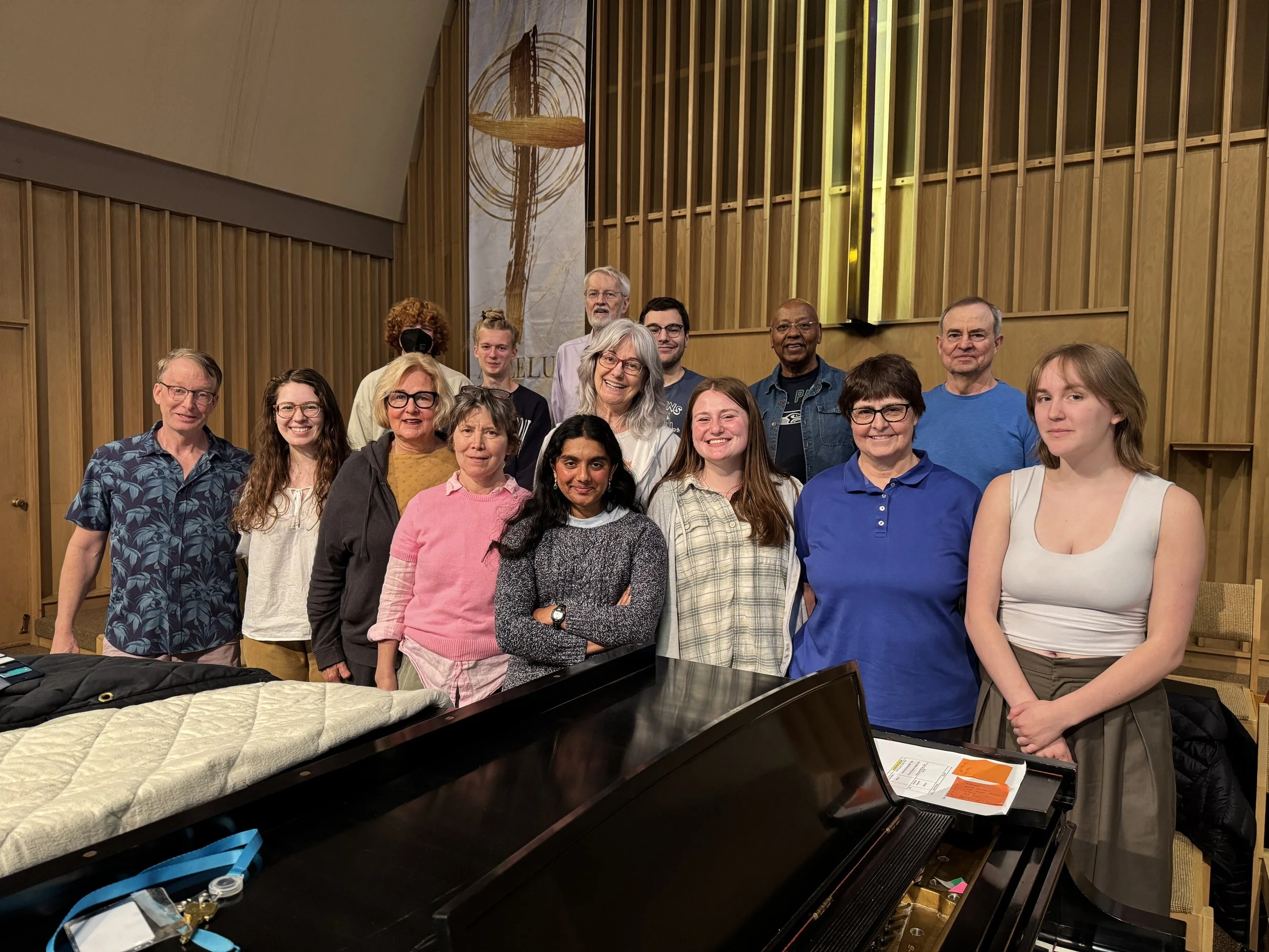 Group of diverse people smiling and posing for a photo inside a wooden church or chapel, with a piano in the foreground.