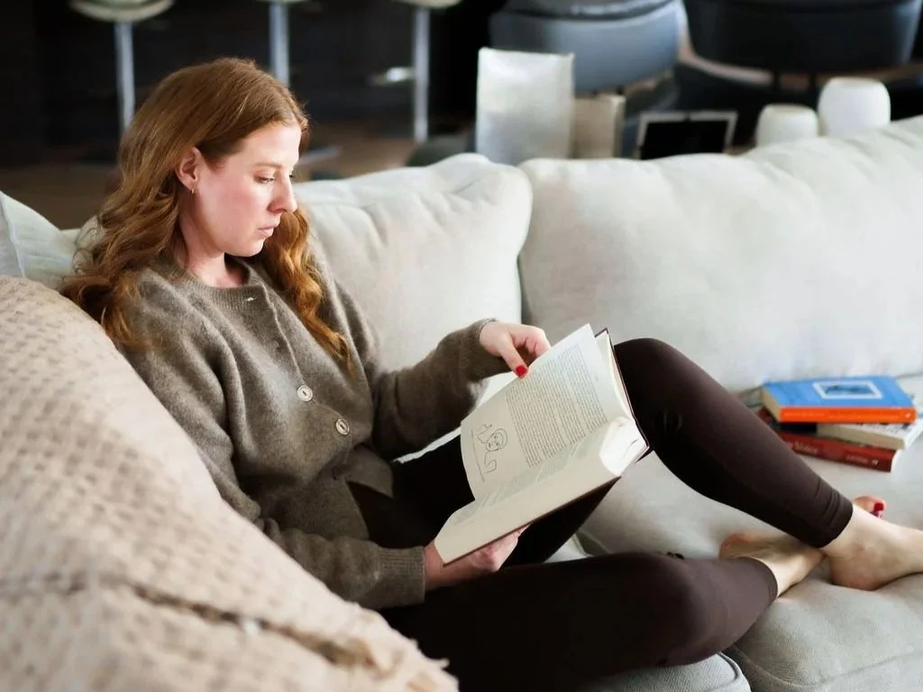 Nicole Lenkeit, trauma therapist and Pilates of pain and stress recovery in Sacramento CA, sitting on the couch reading a book about EMDR.
