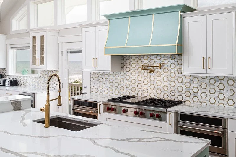 Modern kitchen with white cabinets, a honeycomb tile backsplash, a large island with marble countertop, and mint green range hood.