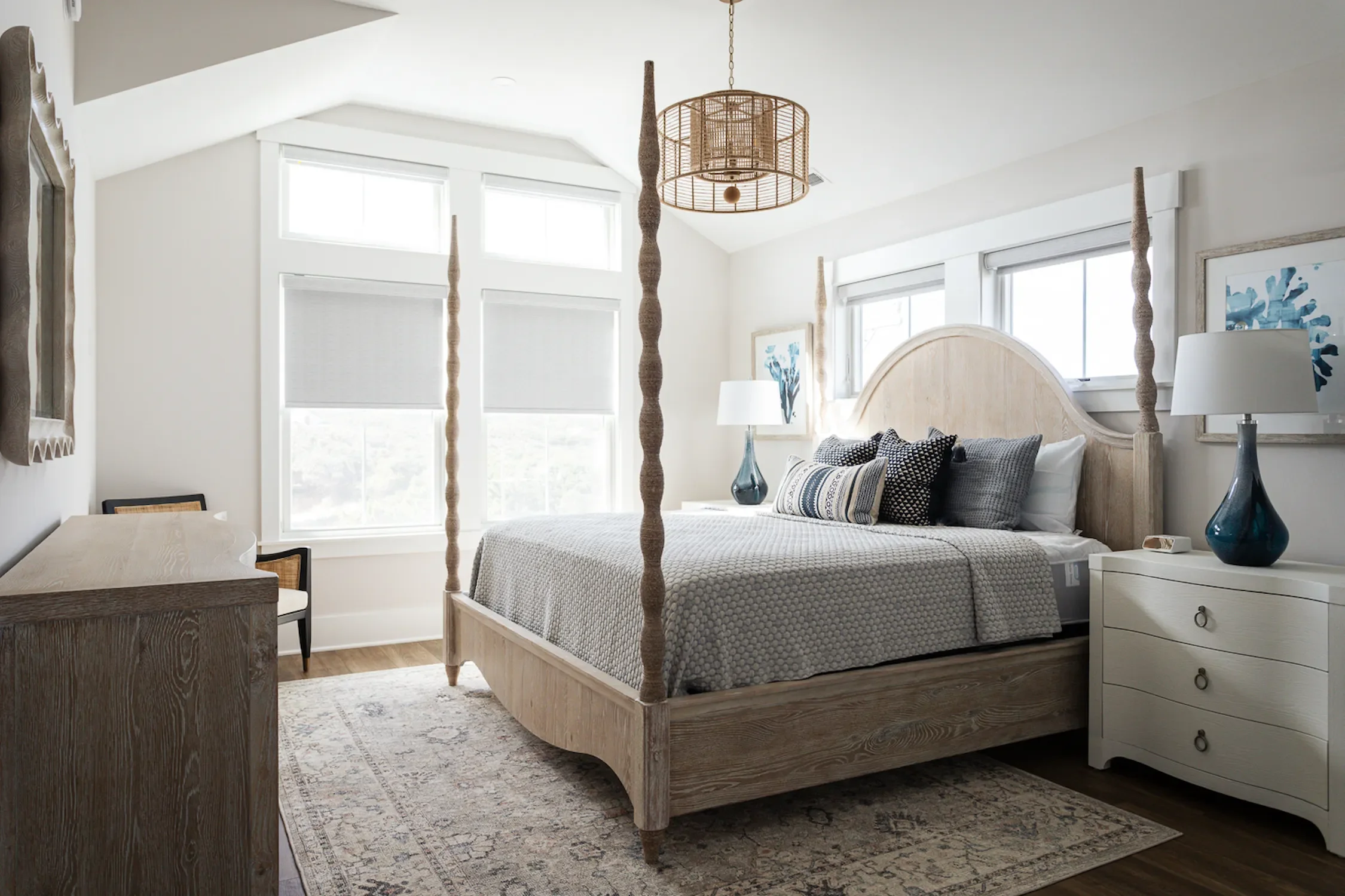 A bedroom with a four-poster wooden bed, white walls, large windows, and a beige and white rug.