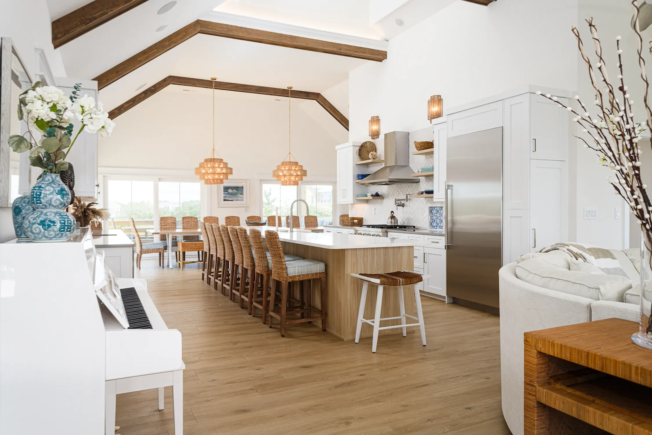 Open-concept kitchen and dining area with white cabinetry, stainless steel appliances, a large island with seating, wicker chairs, and wood accents.