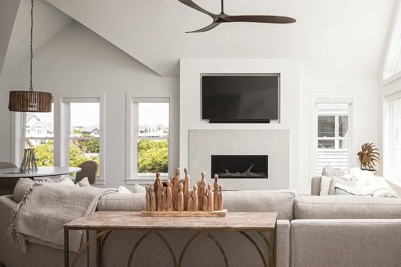 Living room with a large sectional sofa, fireplace, wall-mounted TV, and multiple windows showing a neighborhood view.