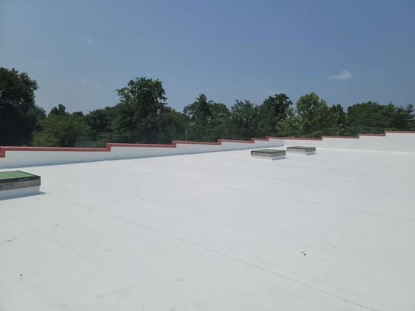 View of a white flat roof with few air vents, surrounded by green trees and a partly cloudy sky.