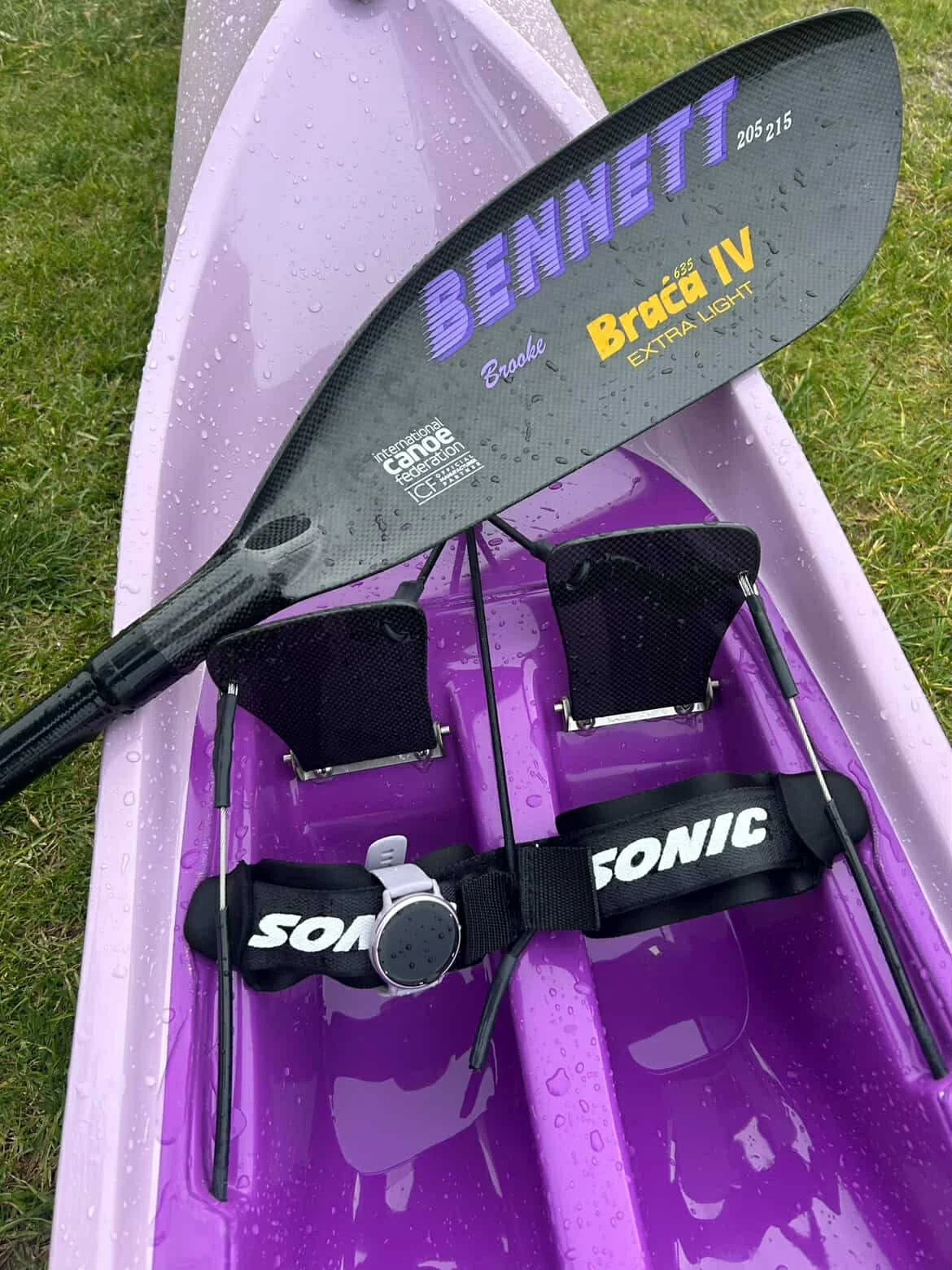 A purple kayak with a black paddle that reads 'Benett Braca IV Extra Light' resting against a SONIC Ski