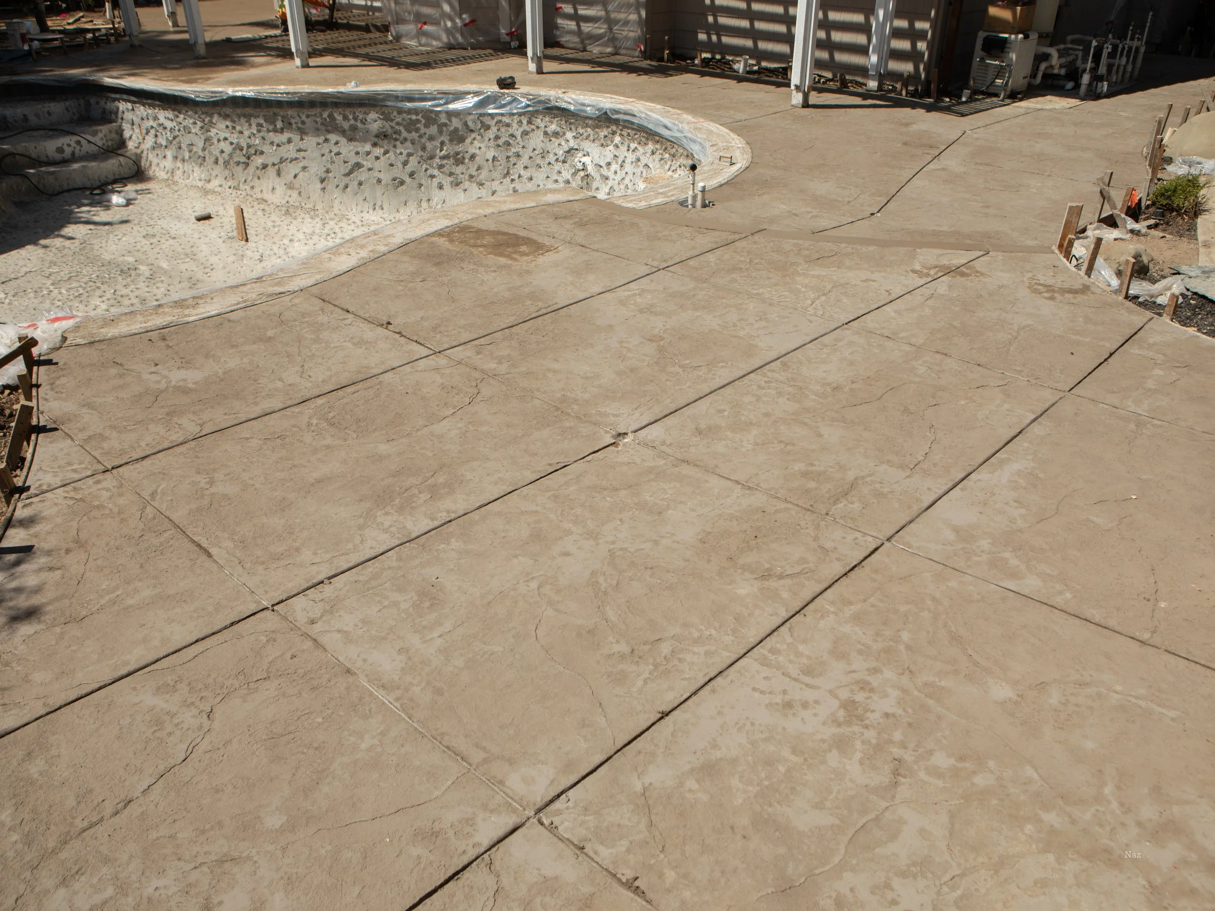 Construction site with freshly poured concrete flooring, a bathtub surrounded by gravel, and construction materials including wood and plastic sheets.