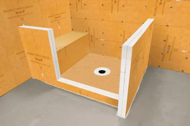 A partially built shower stall with orange drywall, a circular drain in the floor, and white framing on the front corners.