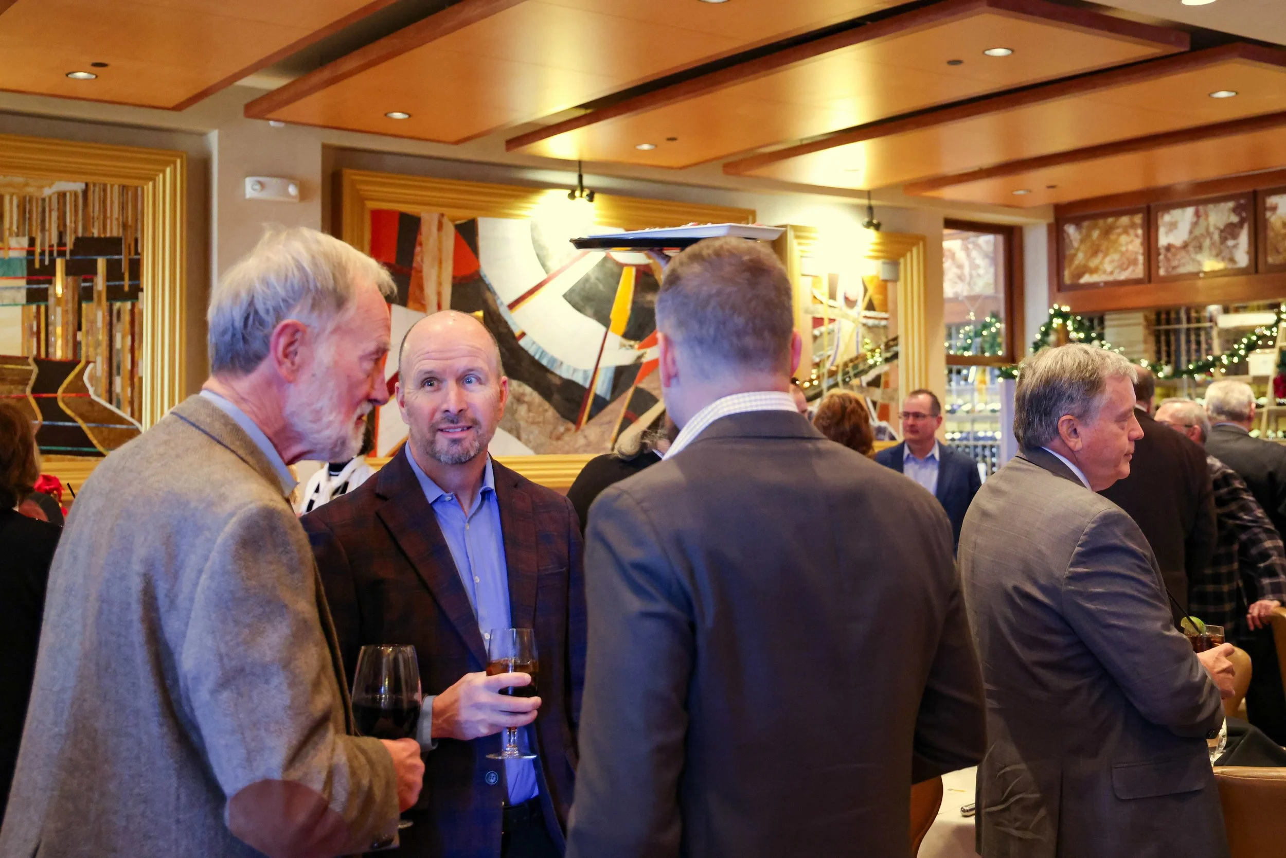 People socializing at a formal event, chatting and holding glasses of wine, in a decorated indoor setting.