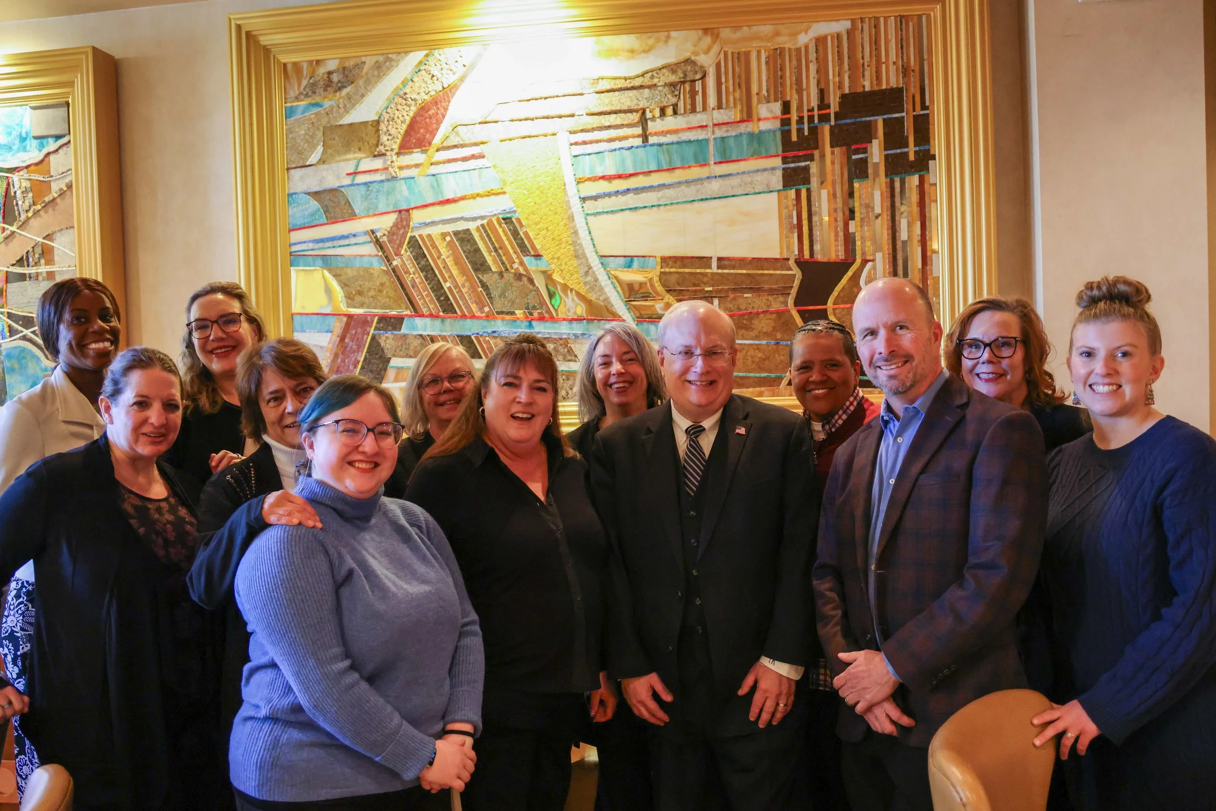 Group of people smiling and posing for a photo in a room with colorful abstract artwork on the wall behind them.