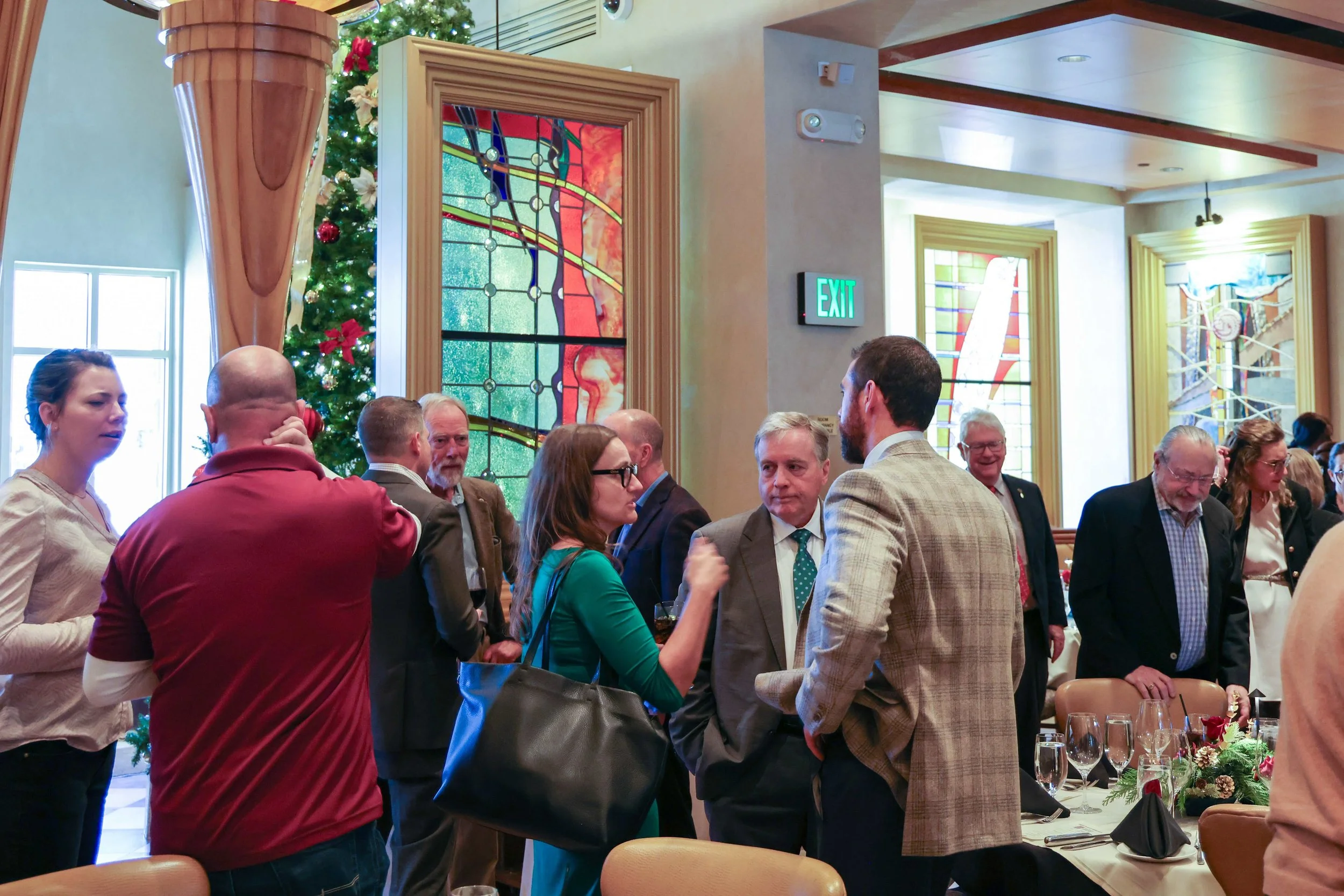People socializing at a festive gathering in a decorated room with stained glass windows and a Christmas tree.