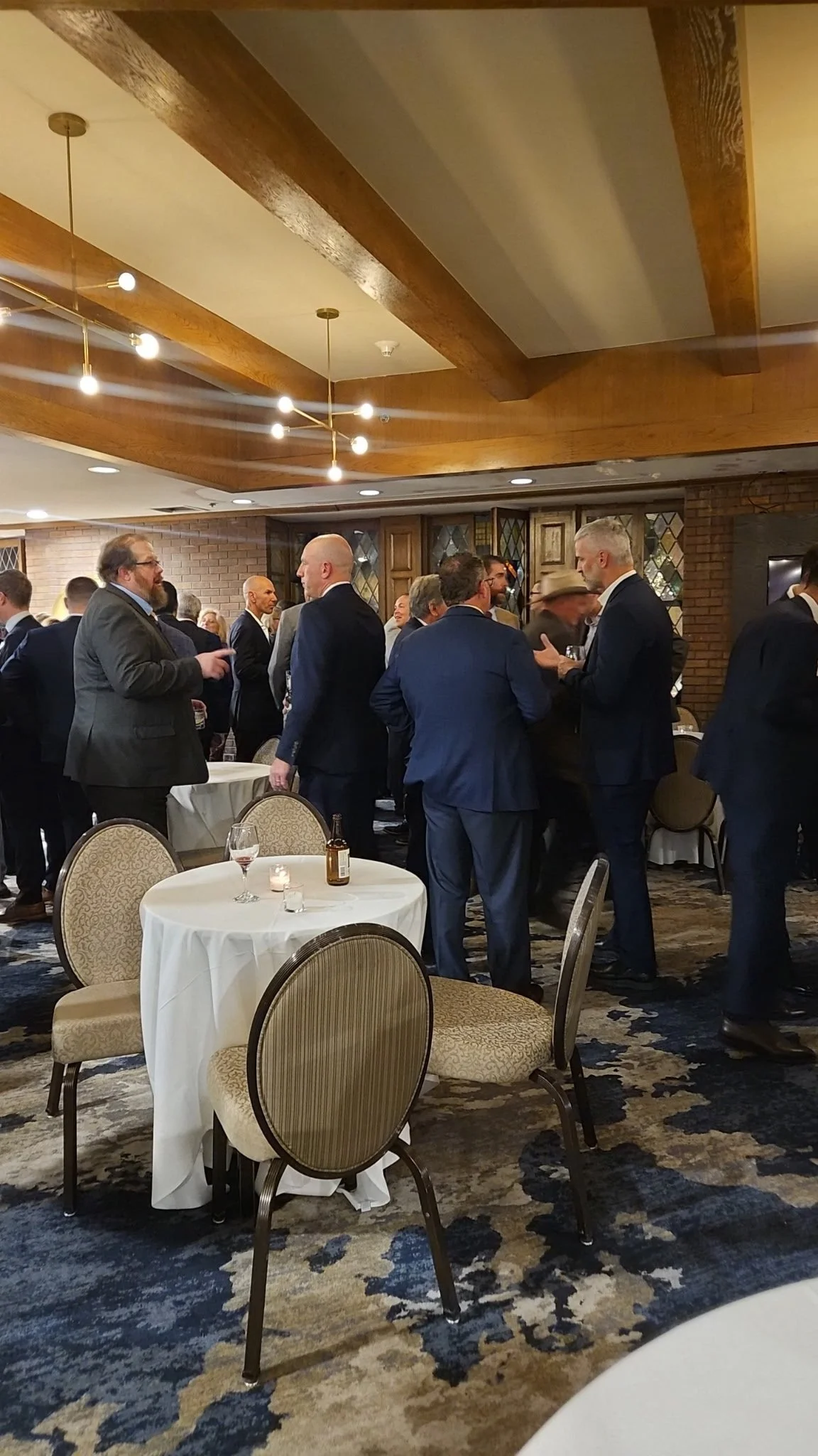 A group of men in suits socializing and conversing at a formal event in a banquet hall.