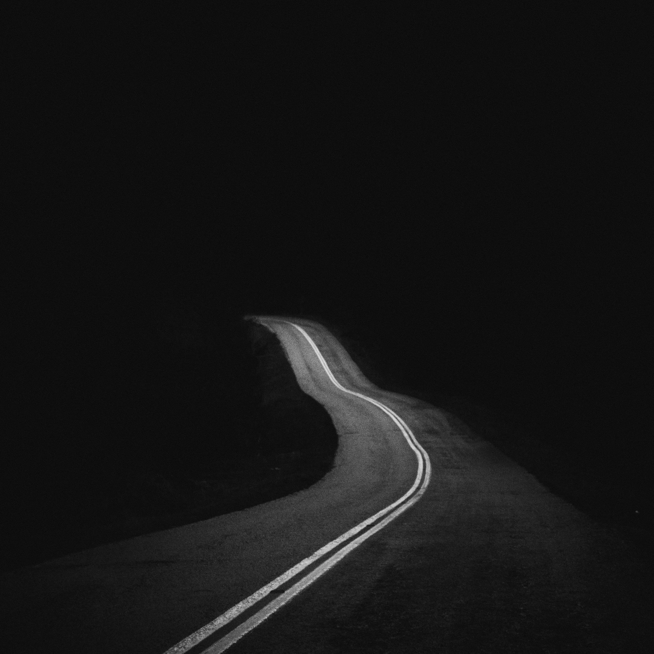 A winding road with double yellow lines disappearing into darkness, with no visible surroundings.