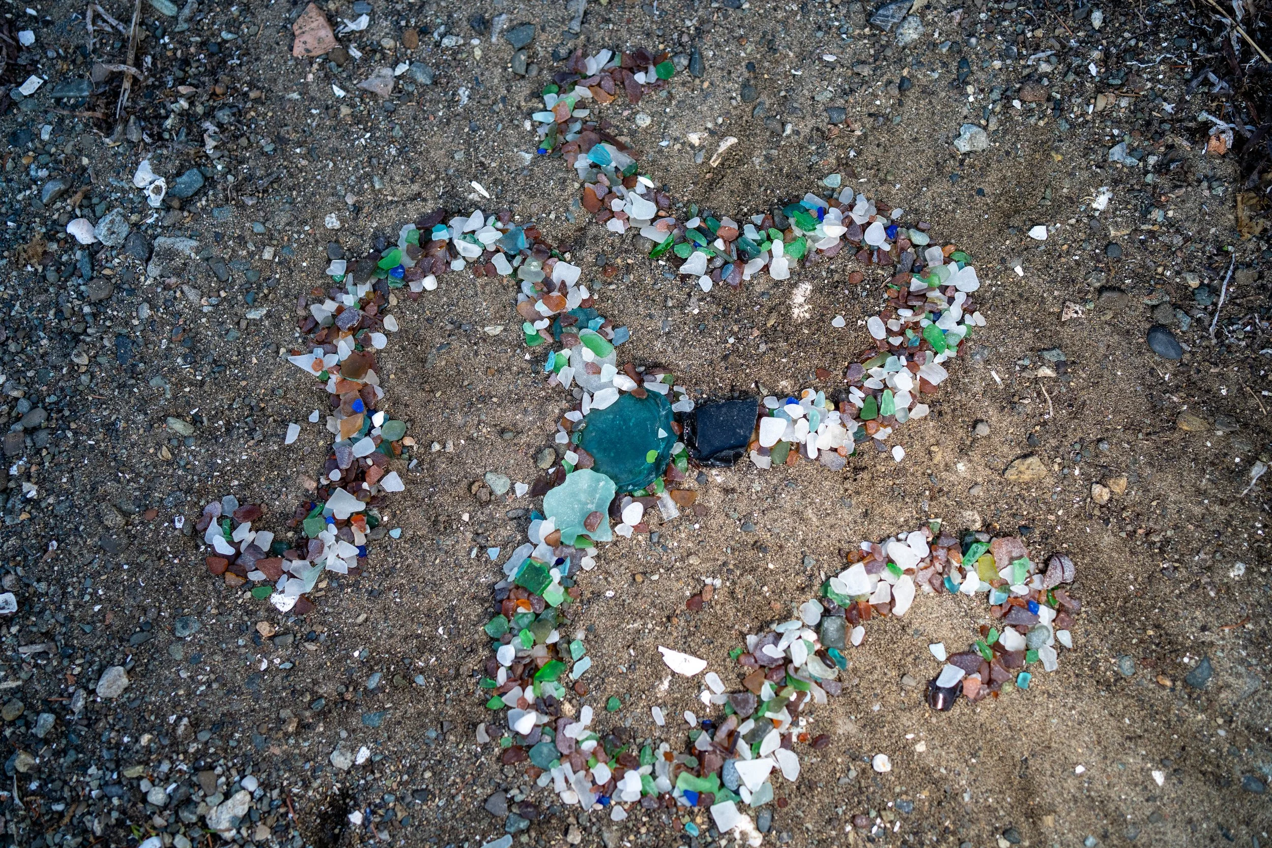 Beach with a starfish shape outlined in small pieces of colorful sea glass and shells.
