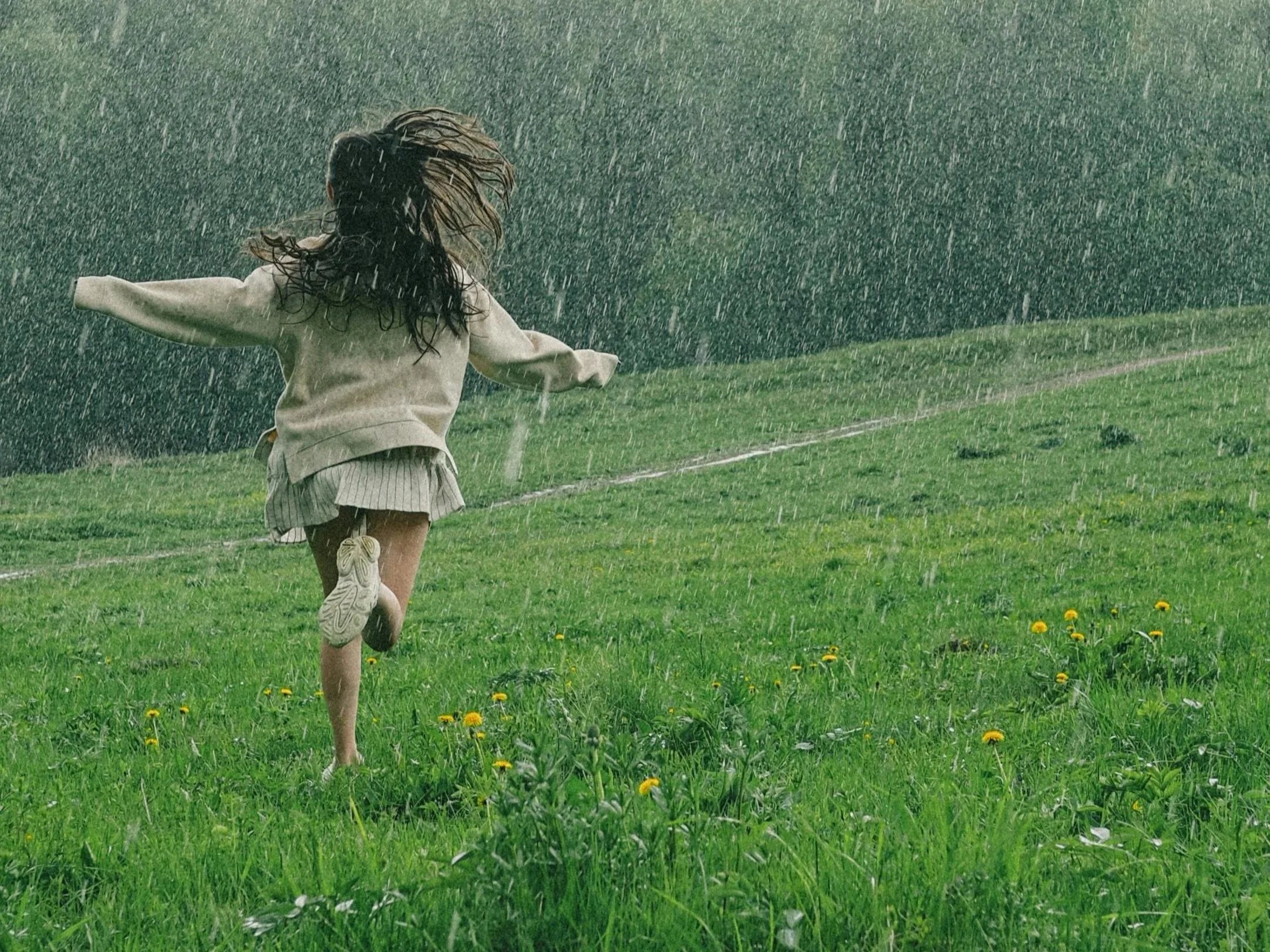 Child running in a grassy field during a rainstorm with rain pouring down.