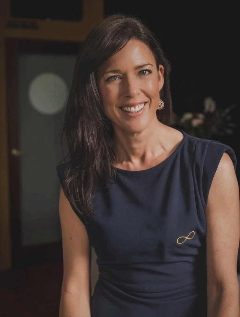 Founder Natalie Bell of Infinity Infusions portrait image. Natalie has long brown hair and is wearing a blue top with the Infinity Infusions gold infinity logo symbol.