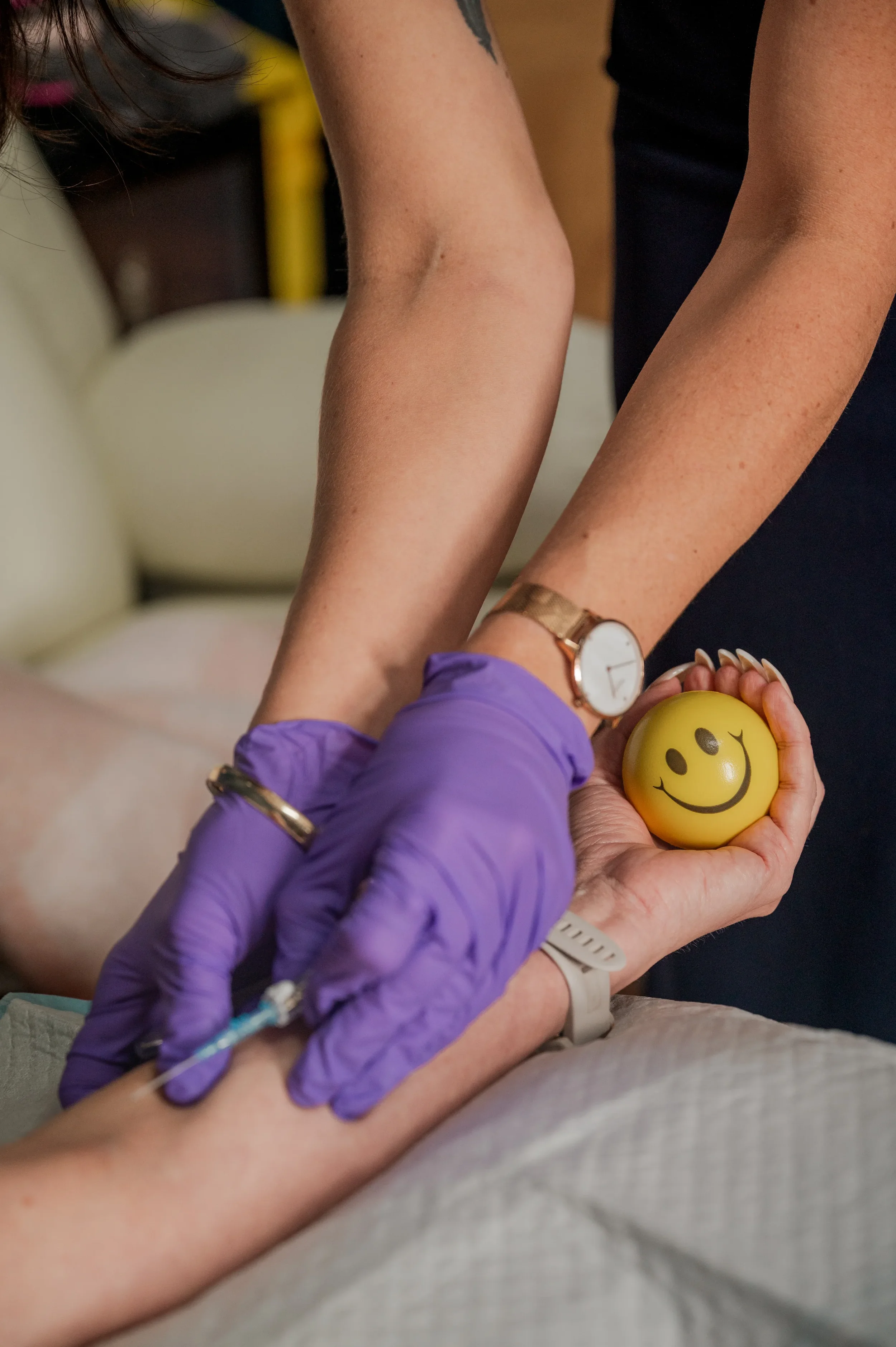 Registered Nurse Natalie Bell administering IV Therapy injection wearing purple medical gloves.