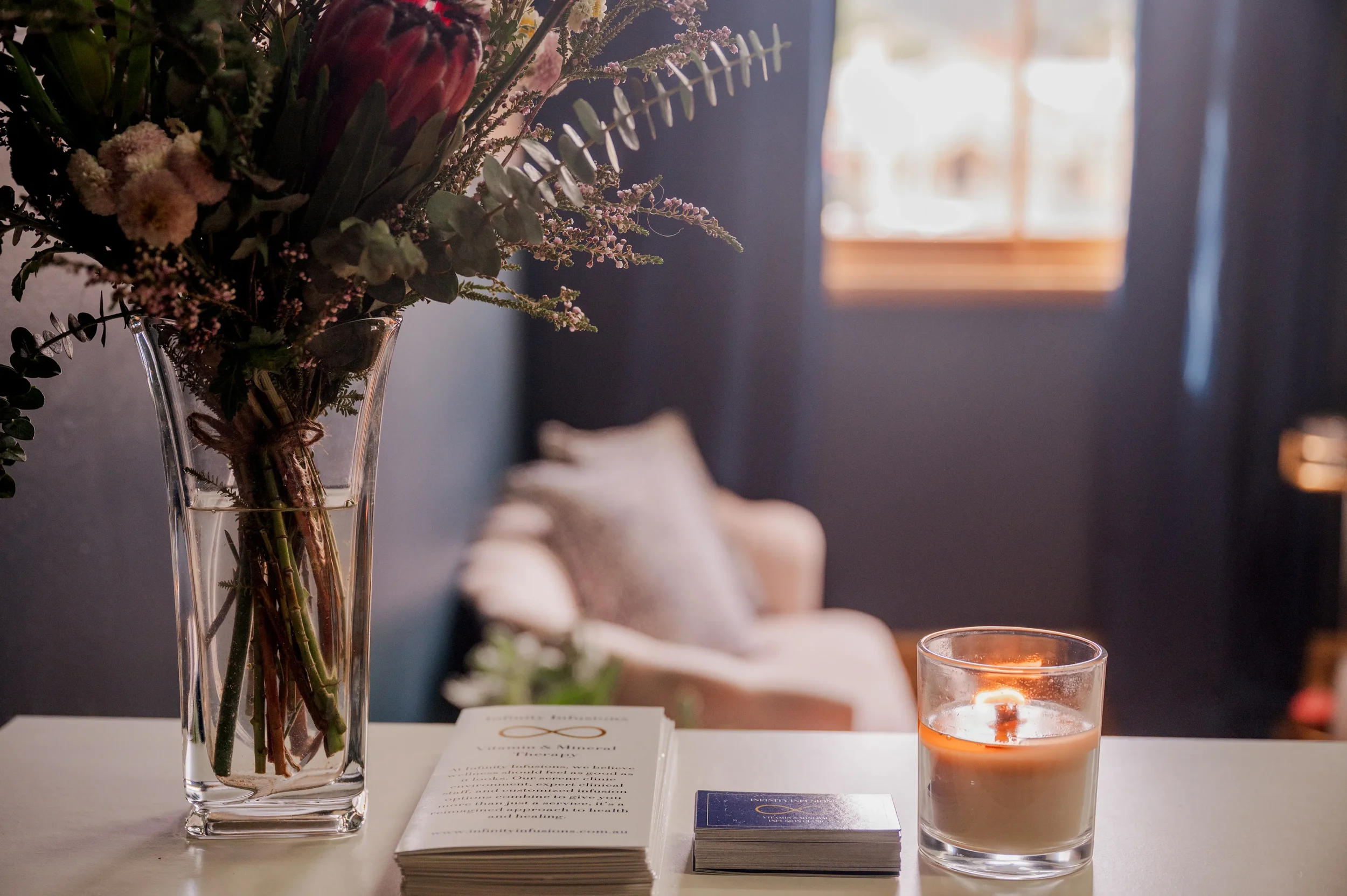 Infinity Infusions clinic space with business cards, flyers, candle and flowers in vase on counter.
