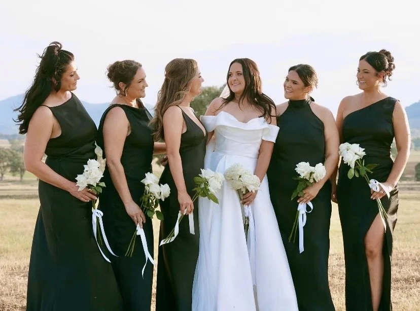 A happy bride is looking at her bridesmaids as they stand together with white rose bouquets.