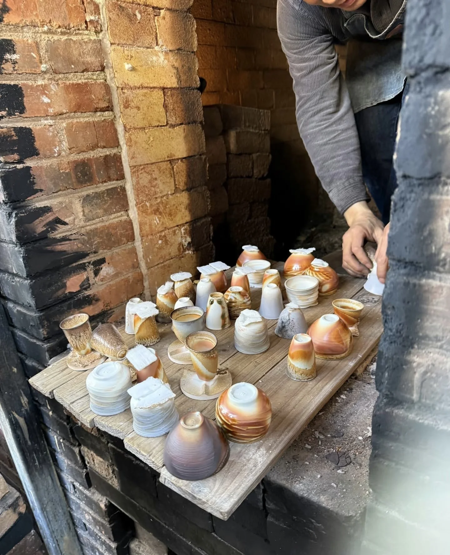 A person arranging a collection of seashells on a wooden table inside a brick fireplace or oven.