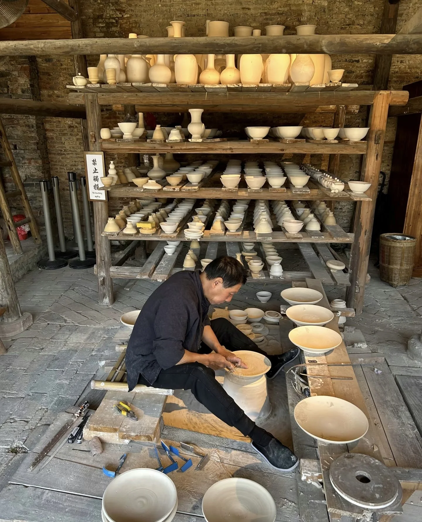 A person working on a pottery wheel, crafting a ceramic bowl in an artisan studio with shelves filled with various unfinished pottery pieces.