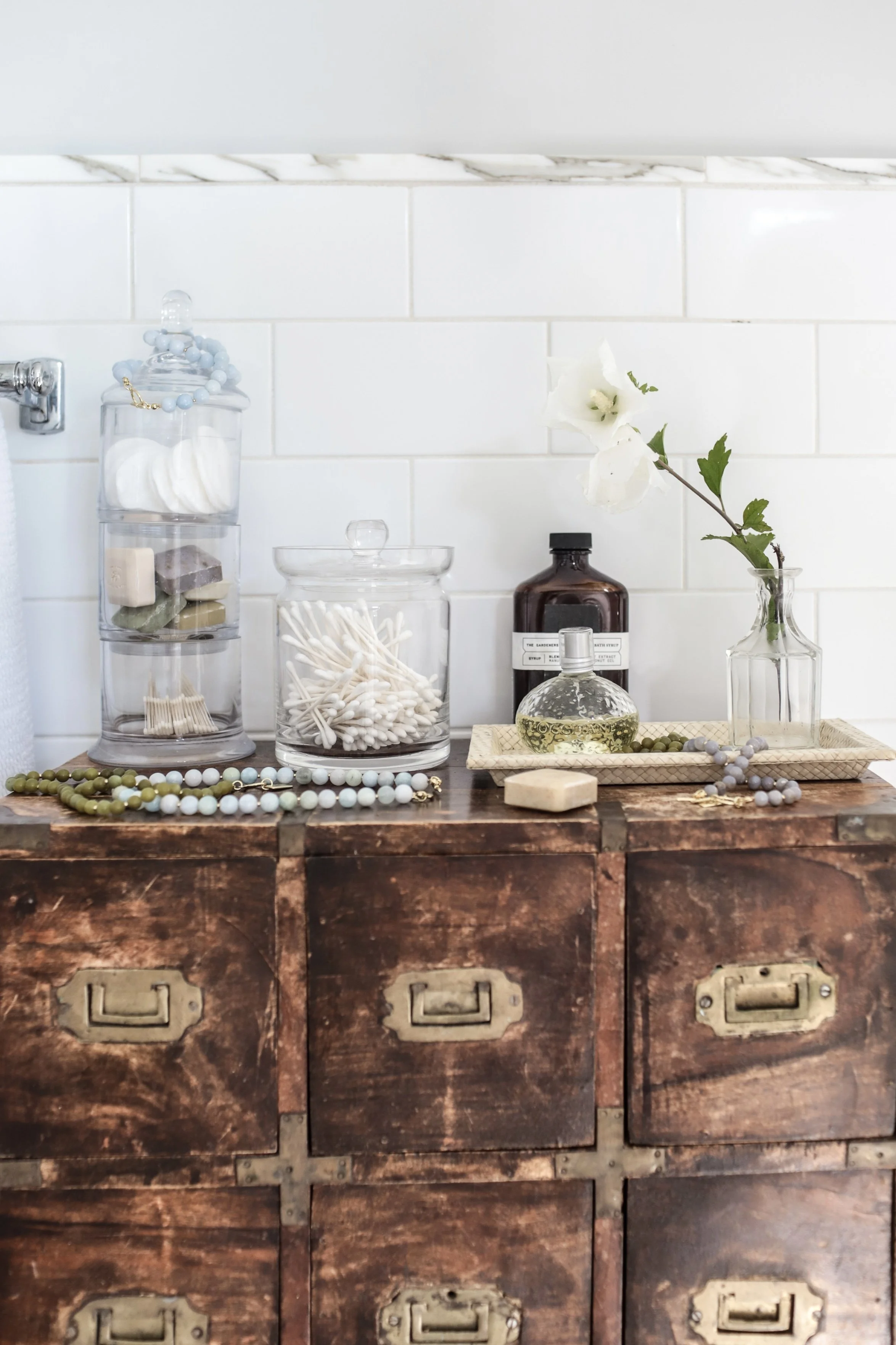 Antique bathroom cabinet with flowers, glass jars, soap, and Lomi necklaces scattered throughout.