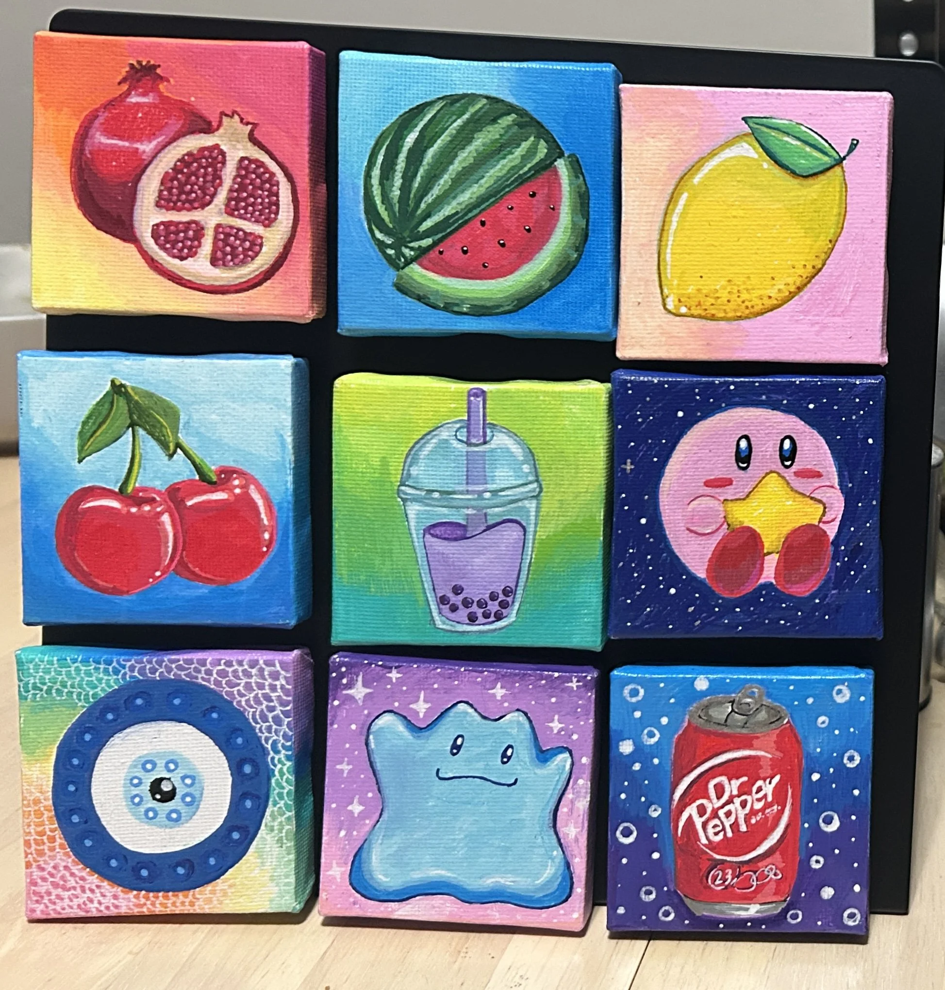Nine small colorful paintings of various objects and characters on a black background. The images include pomegranates, a watermelon, a lemon, cherries, a bubble tea, Kirby holding a star, a Pokéball, a cute star character, and a can of Dr. Pepper.