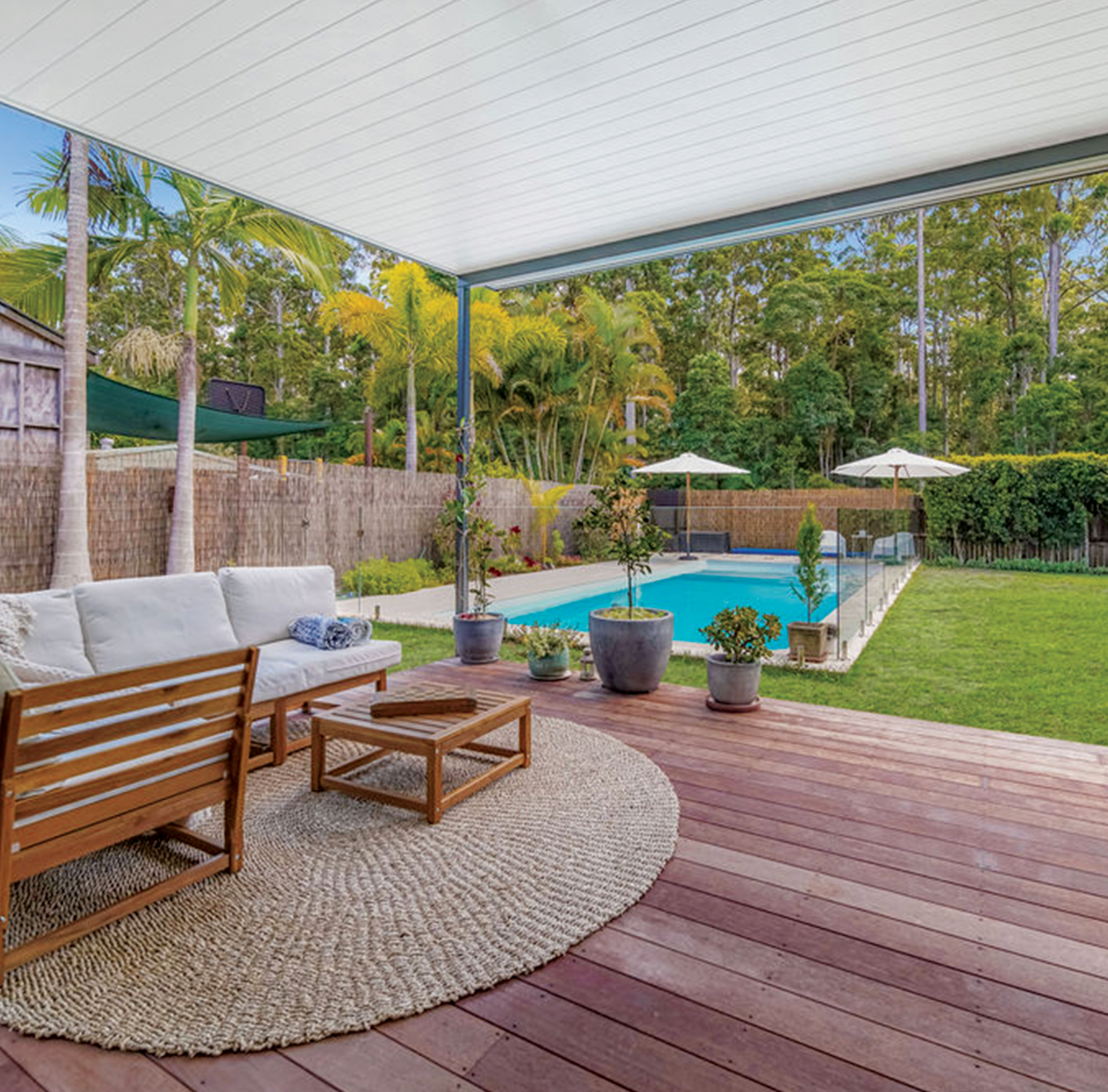 Custom outdoor entertaining area in Brisbane, Queensland, featuring a bespoke deck and pergola complemented by premium glass pool fencing and timber boundary fencing on two sides of the pool. This project also included extensive landscaping and high-