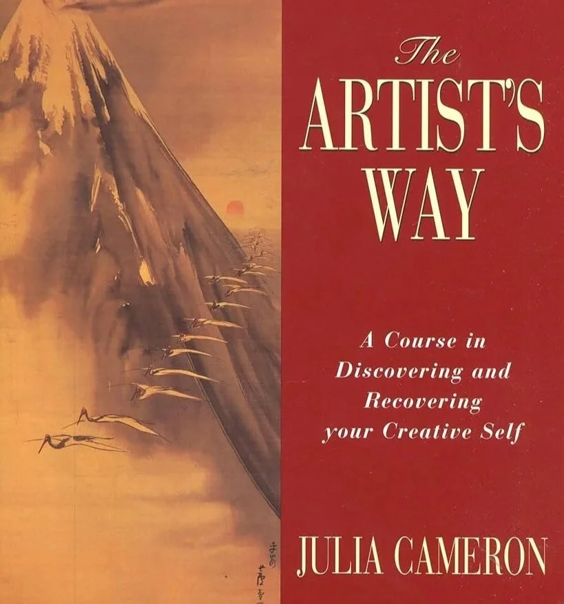 Book cover titled 'The Artist's Way' by Julia Cameron, featuring a painted mountain landscape with a sunset and a small boat on water.