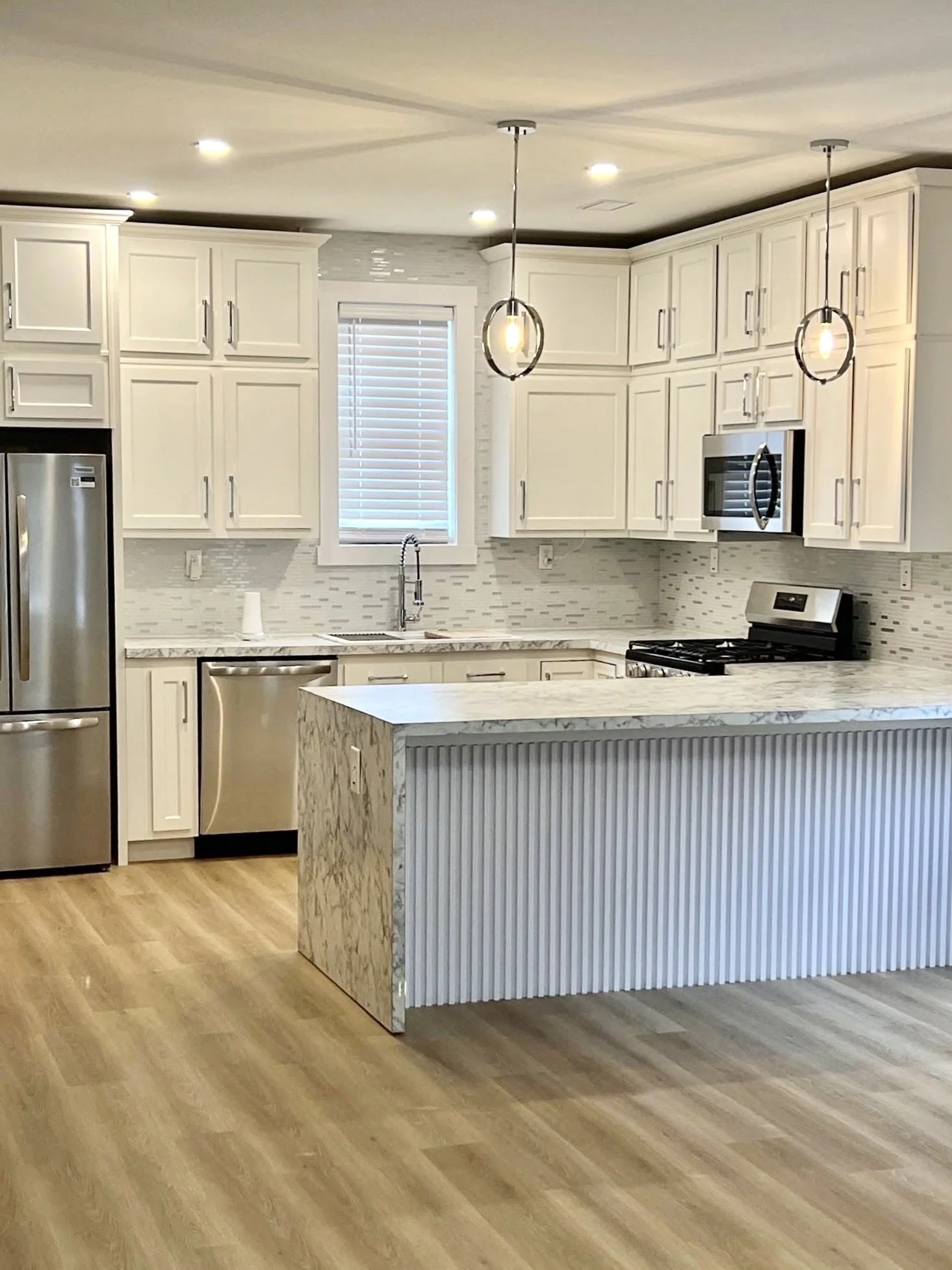 Modern kitchen with white cabinets, marble countertops, stainless steel appliances, pendant lights, and wooden flooring.