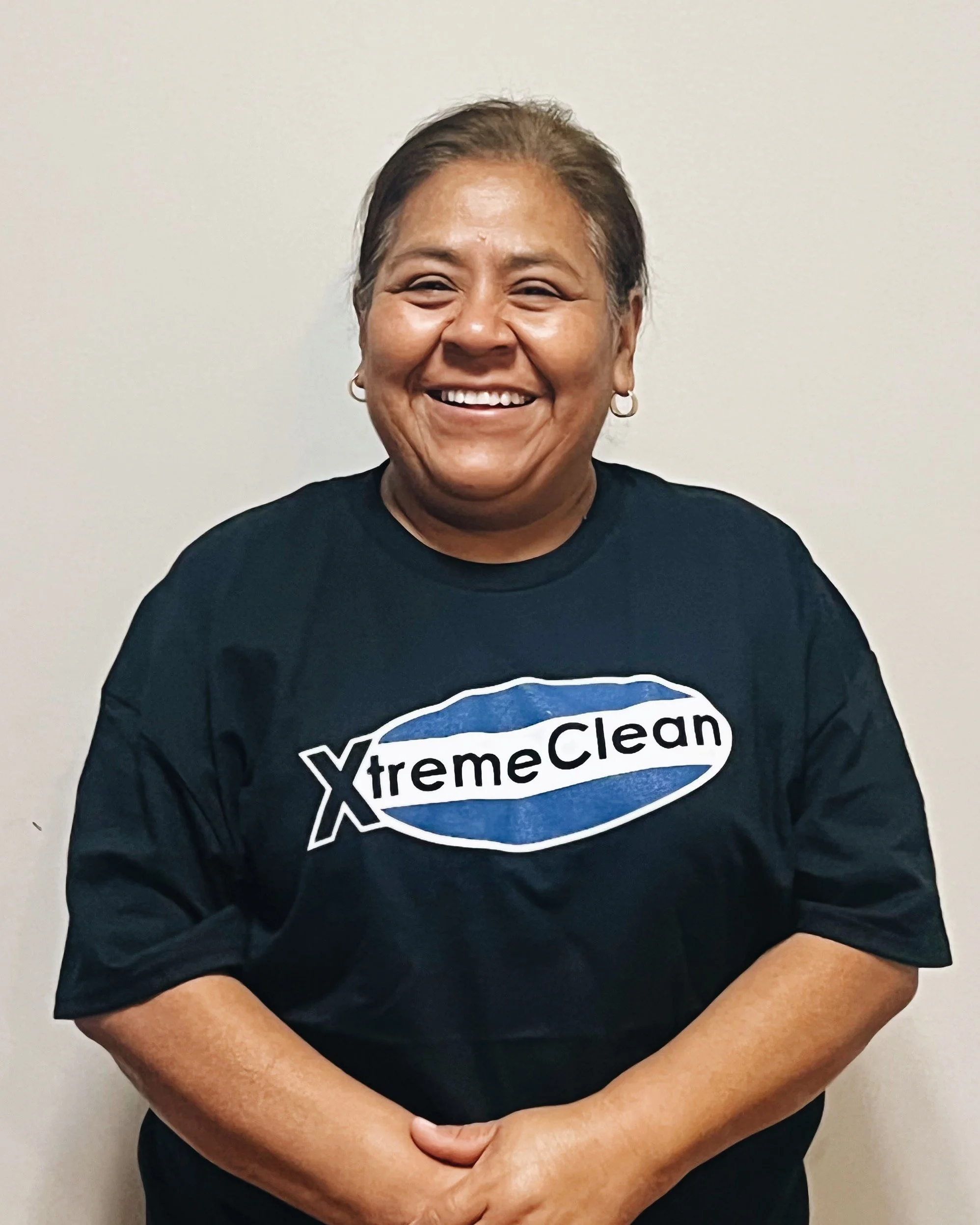 A woman smiling, wearing a black T-shirt with the logo 'XtremeClean' on it, standing against a plain wall.