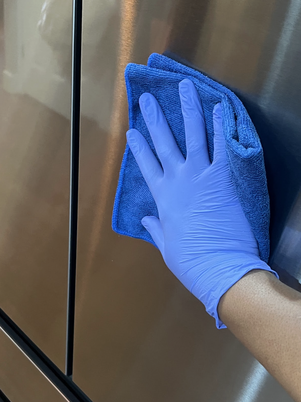 A person wearing a blue glove using a blue microfiber cloth to wipe a metallic surface.