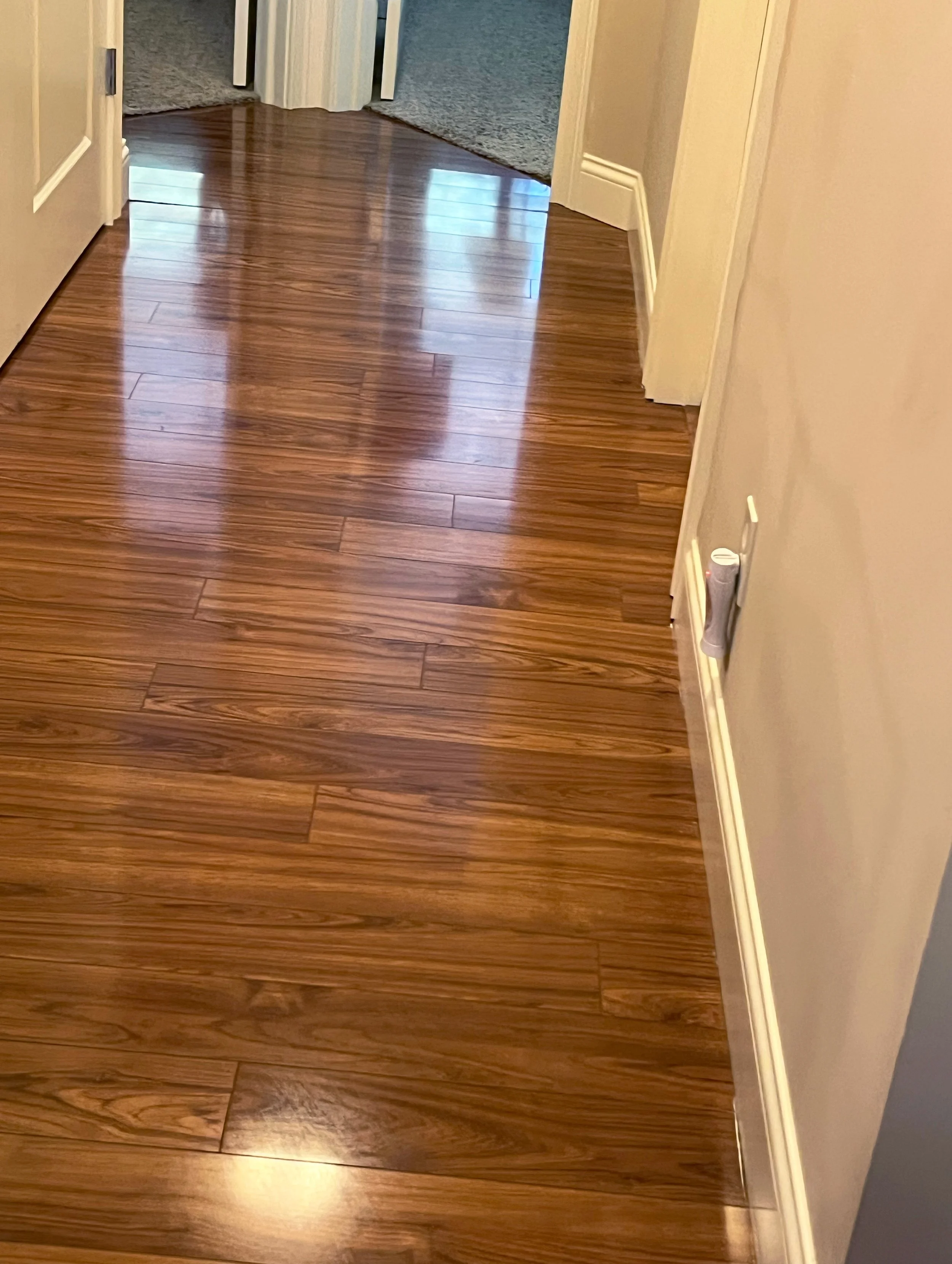Polished, wooden floor in a hallway with a door open at the end.