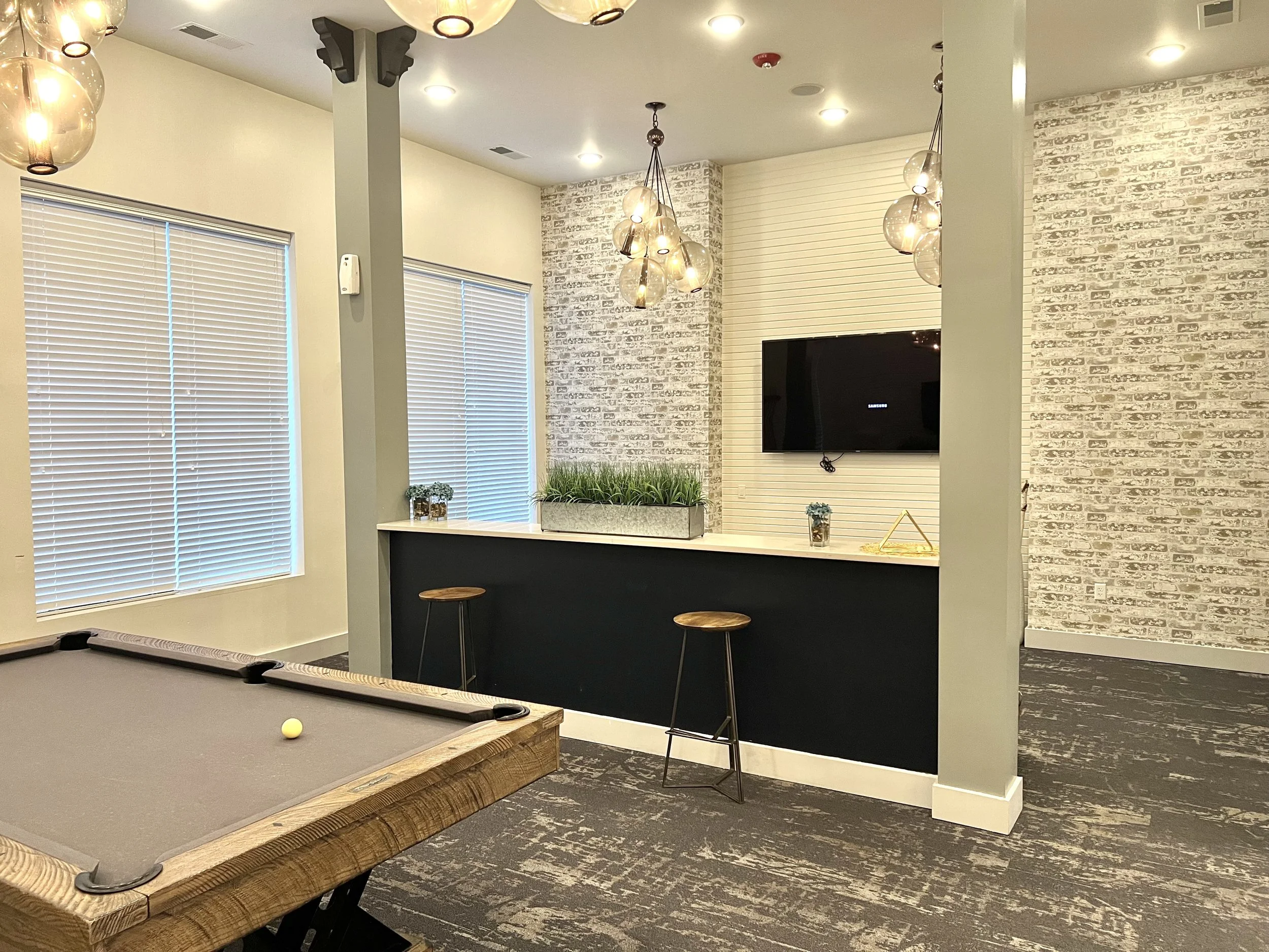 Indoor recreational space with a pool table, bar area, bar stools, wall-mounted TV, and lighting fixtures.