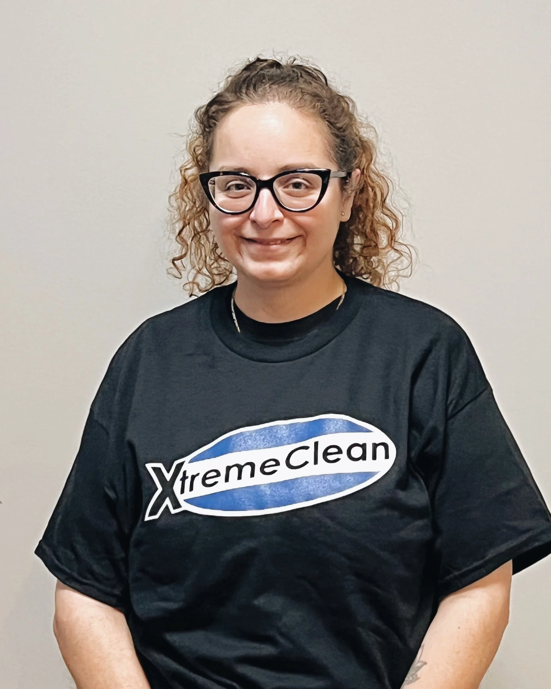 A woman with curly hair and glasses wearing a black T-shirt with 'XtremeClean' logo.