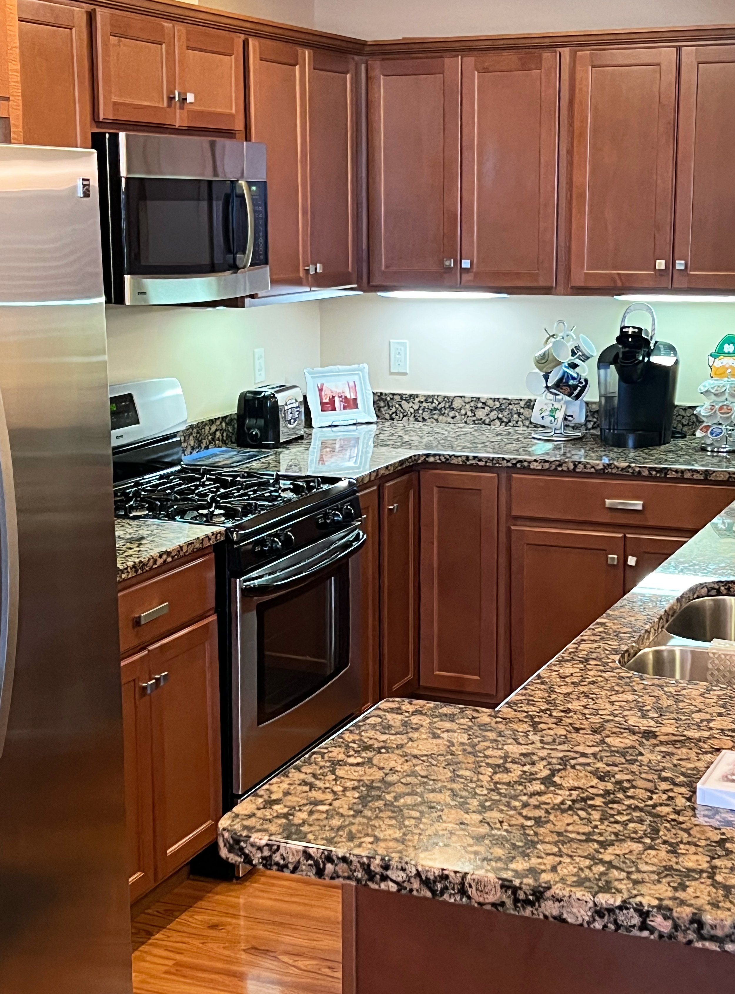 A kitchen with wooden cabinets, stainless steel appliances, a granite countertop, and various small appliances and mugs on the counter.