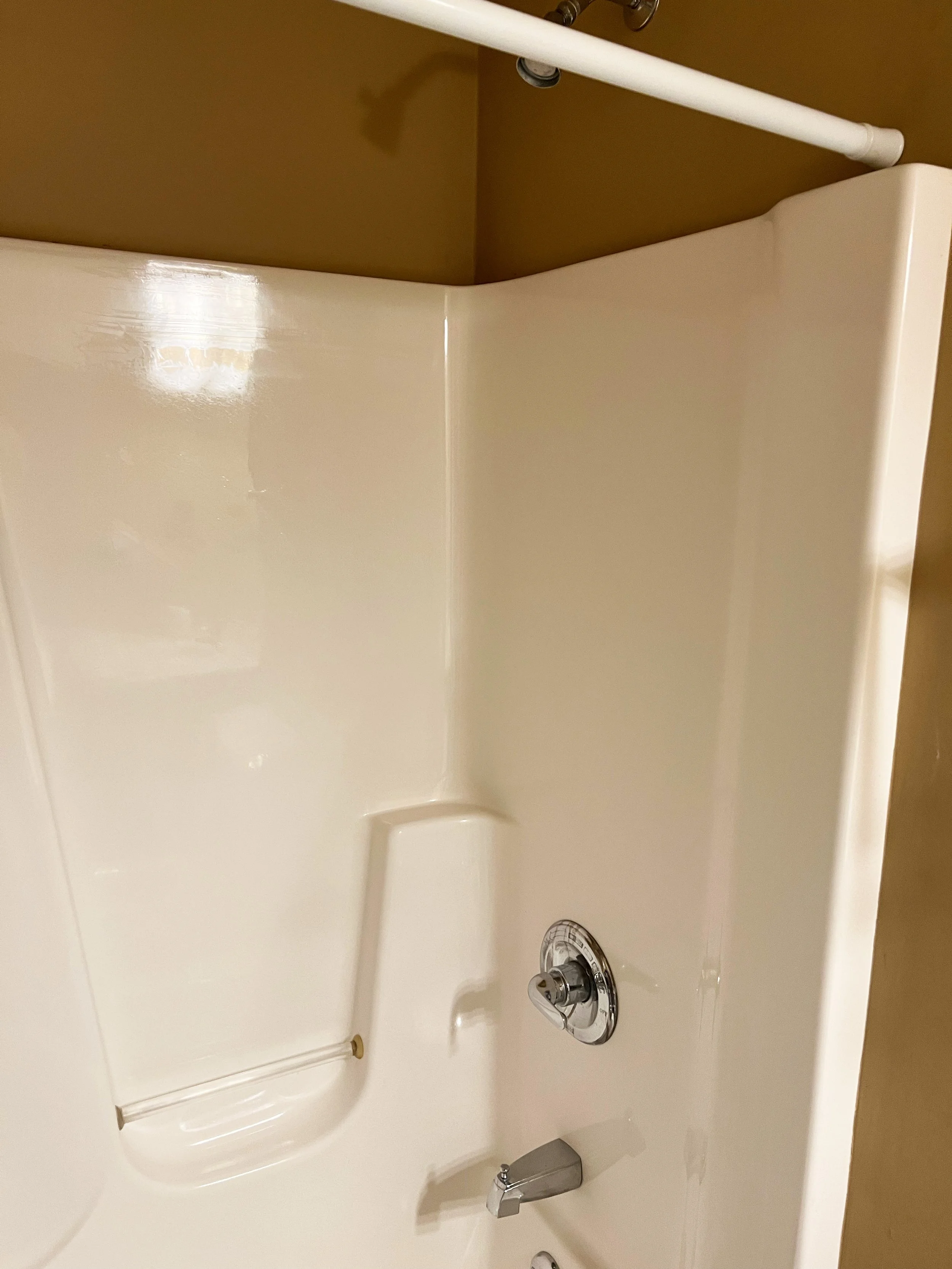 Empty cream-colored bathtub with a built-in seat and a silver shower handle, set against a beige wall.