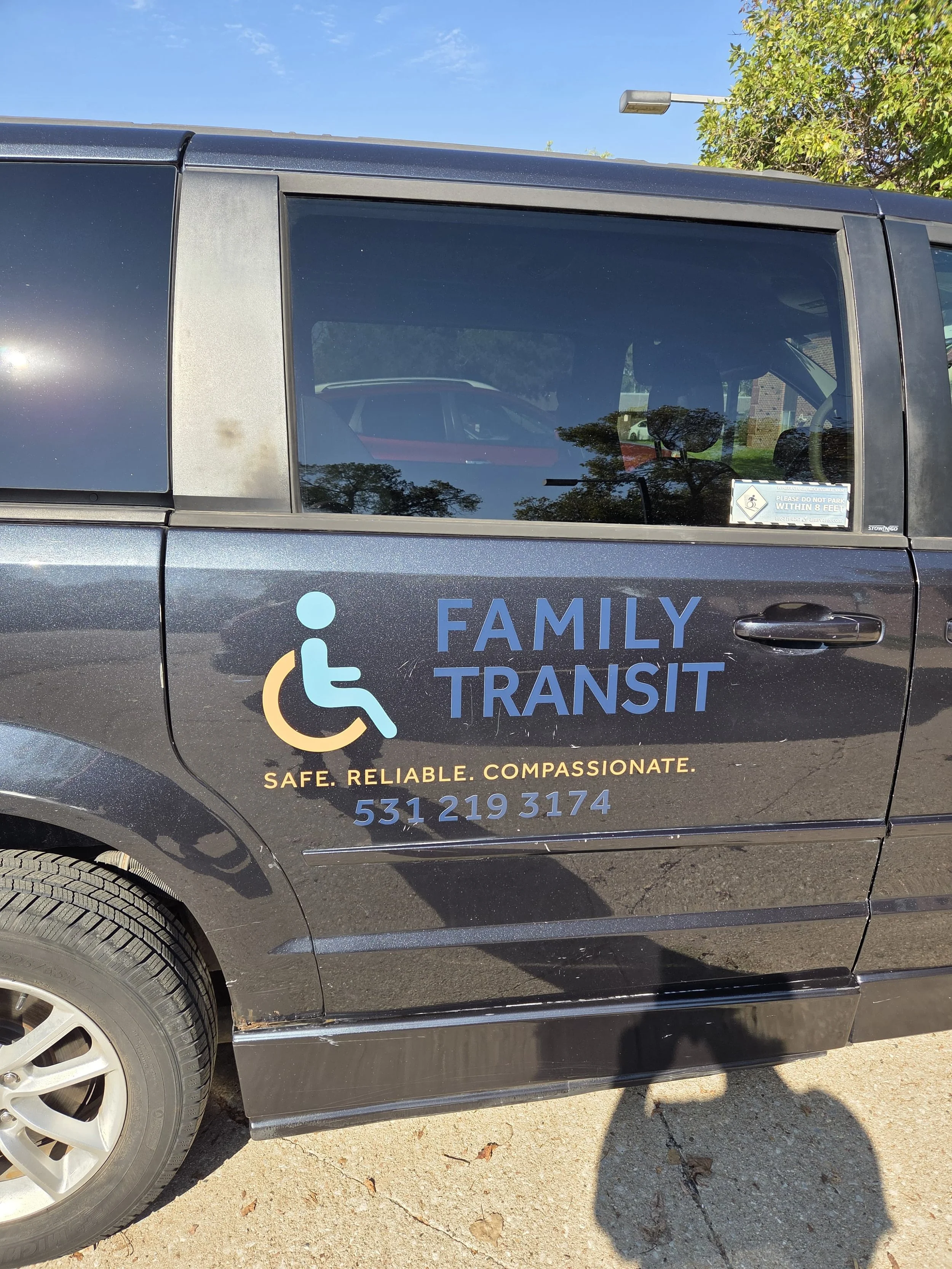 Side of a black Family Transit vehicle with a wheelchair accessibility symbol, company slogan 'Safe. Reliable. Compassionate.' and contact number 531 219 3174.
