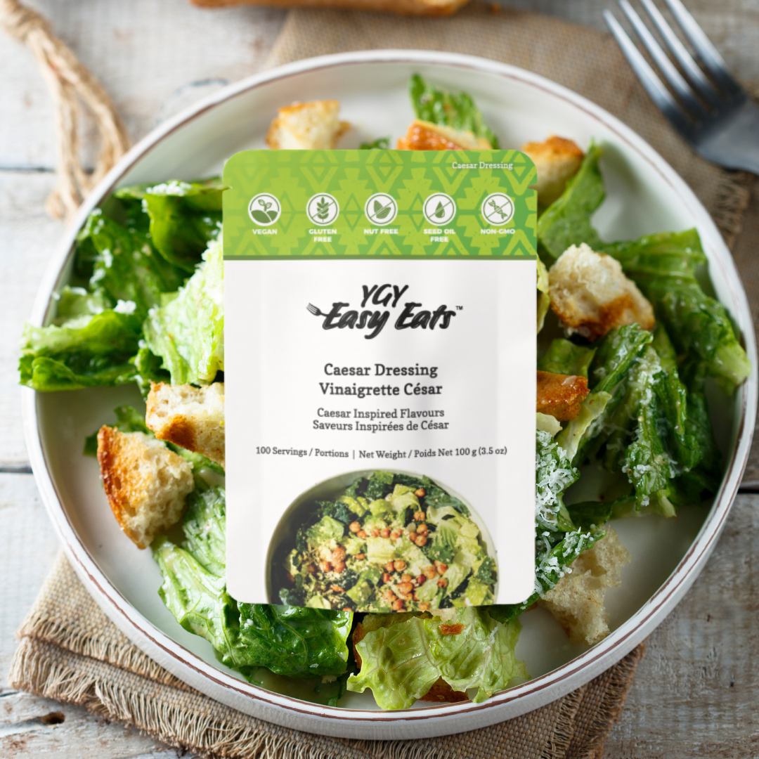 A bowl of Caesar salad with croutons and lettuce, with a packet of YAY Easy Eats Caesar Dressing labeled on top. The packet indicates it is vegan, gluten-free, nut-free, seed oil-free, and non-GMO.