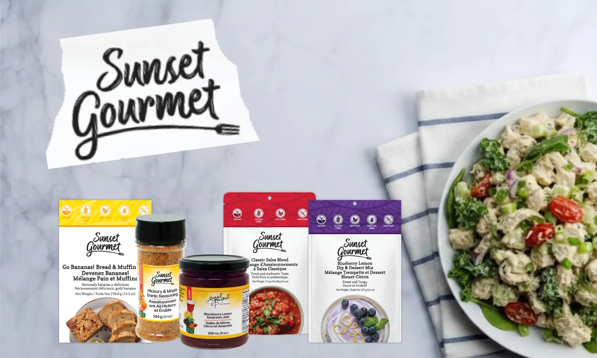 Assorted Sunset Gourmet food packaging including sauces and seasonings on a table next to a plate of salad with cherry tomatoes, broccoli, and chopped vegetables.