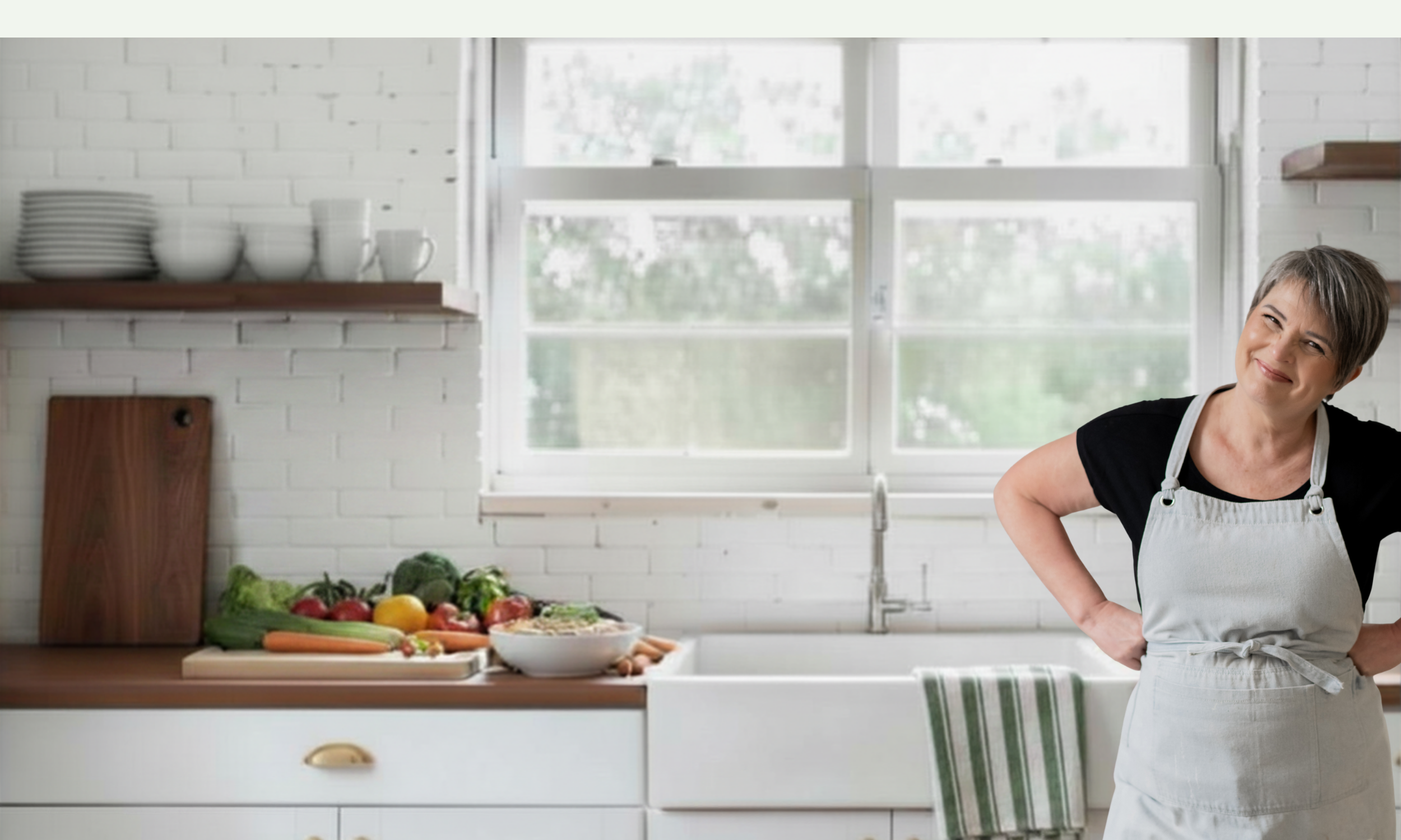 A woman in a white apron stands in a modern kitchen with a smile on her face. The kitchen has a white brick wall, open wooden shelves, and a window with a view outside. On the counter, there are fresh vegetables, a cutting board, and dishes stacked on a shelf.