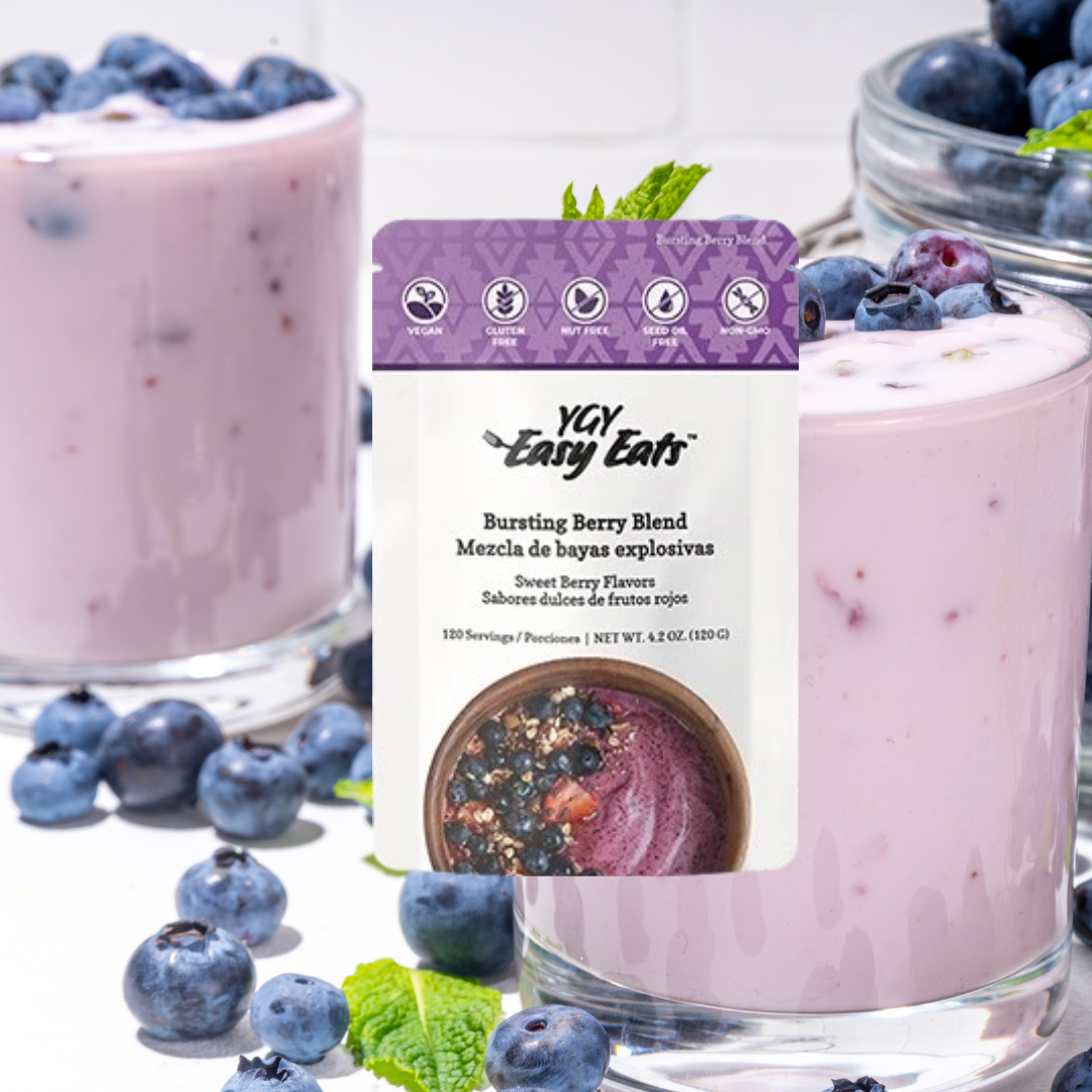 A package of YAY Easy Eats bursting berry blend with blueberries, alongside glasses of blueberry yogurt with blueberries and mint garnishes in the background.