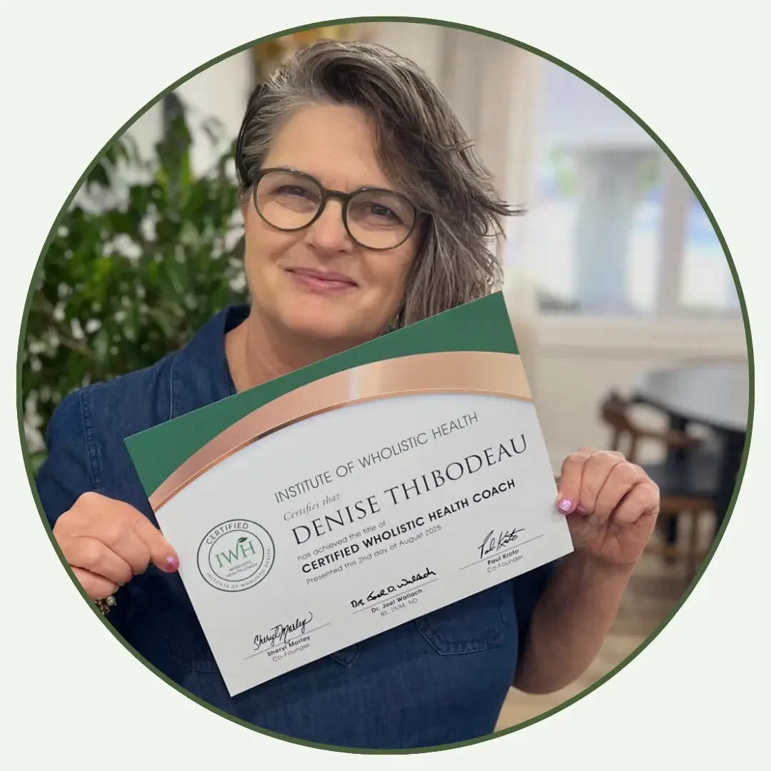 Woman with short gray hair and glasses holding a certificate from the Institute of Wholistic Health, certifying her as a Certified Wholistic Health Coach.