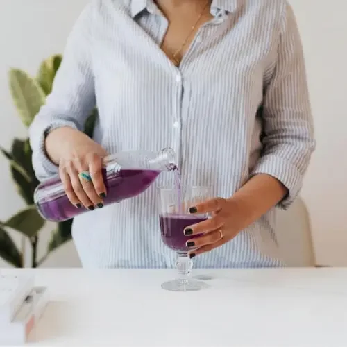 Person pouring a purple immune support beverage into a wine glass.