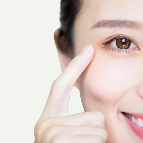 Close-up of a woman's face, showing her brown eye, part of her smile, and her finger pointing at her temple.