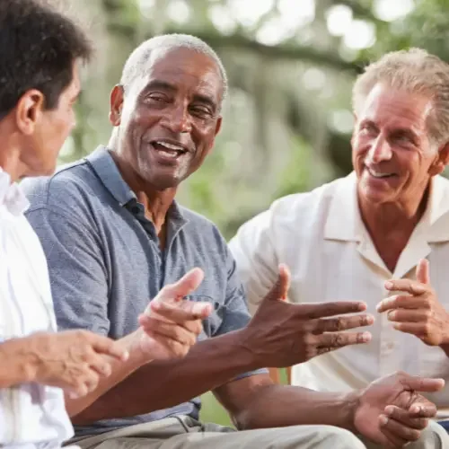 Three men outdoors engaging in a lively conversation, smiling and gesturing.