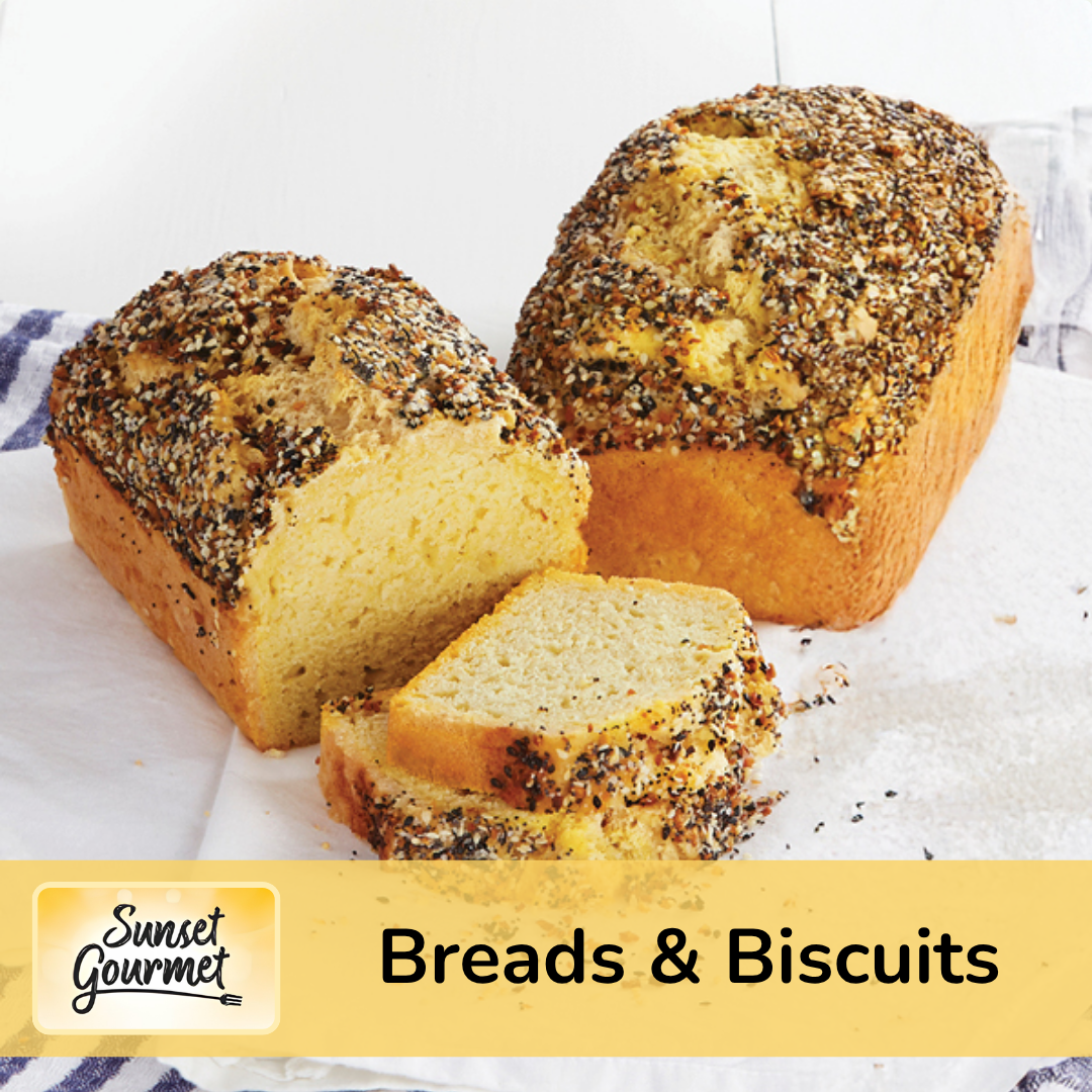 A loaf of vanilla cake with a crumbly topping, partially sliced to reveal its soft, yellow interior, placed on white parchment paper with a label reading 'Breads & Biscuits' and the Sunset Gourmet logo.