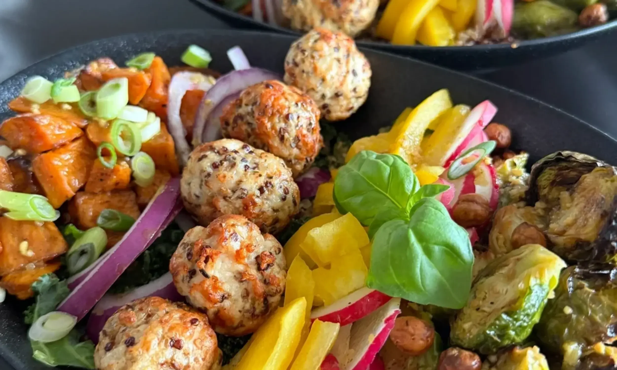 A close-up view of a platter containing various colorful food items including meatballs, sliced onions, bell peppers, radishes, and garnishes like chopped green onions and basil leaves.