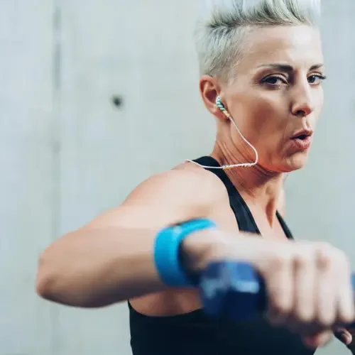 Woman with short gray hair exercising with dumbbell at gym to keep her bone and joints strong.