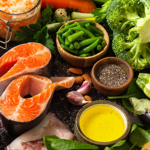 Fresh salmon, green beans, broccoli, garlic, almonds, herbs, and oil on a dark surface.