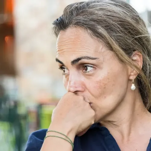 Close-up of a woman with long hair and hoop earrings, resting her chin on her hand and looking to the side with a pensive expression wondering about her brain health.