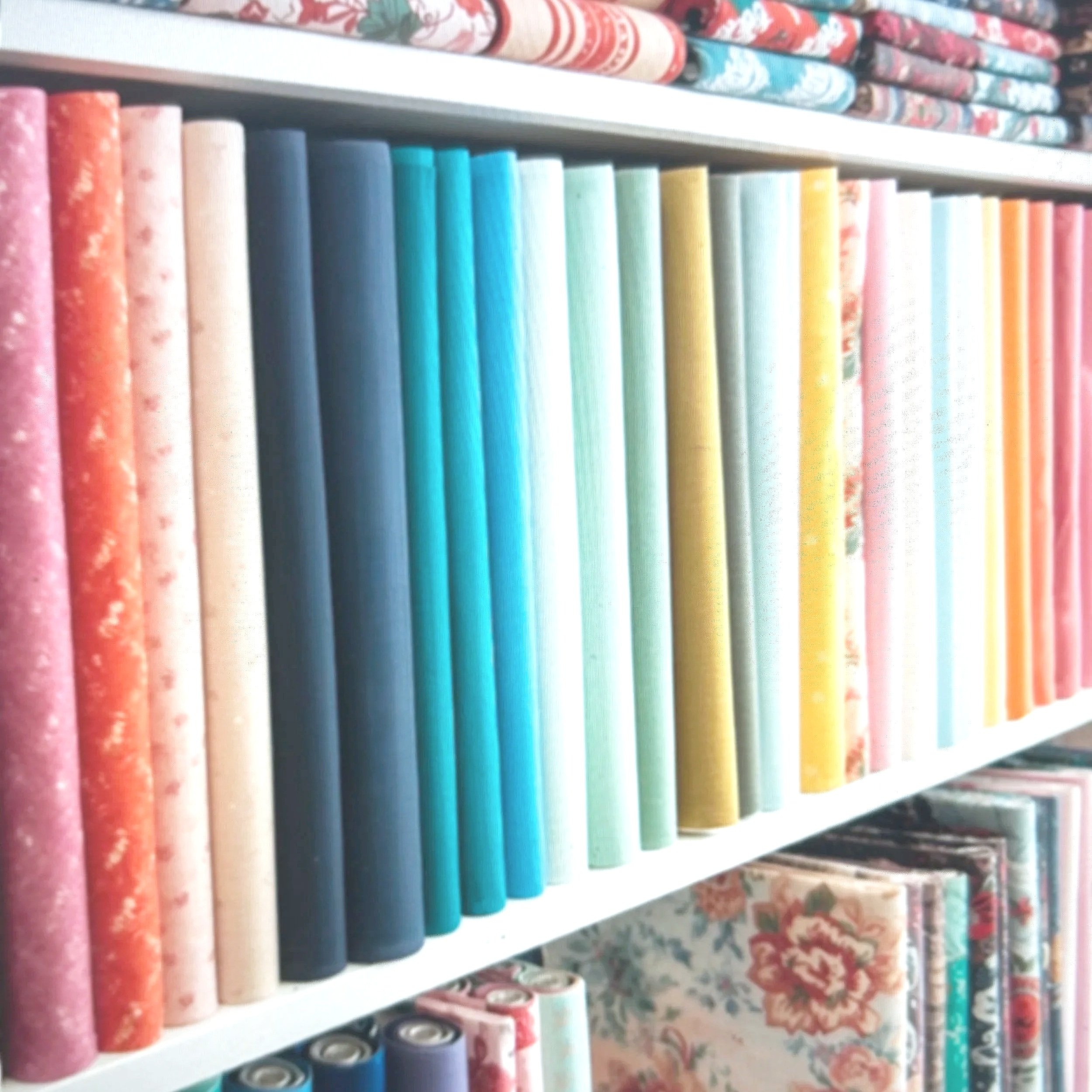 Shelves filled with neatly arranged rolls of colorful fabric in pastel shades including pink, blue, yellow, and green, with some patterned fabrics on top and below.